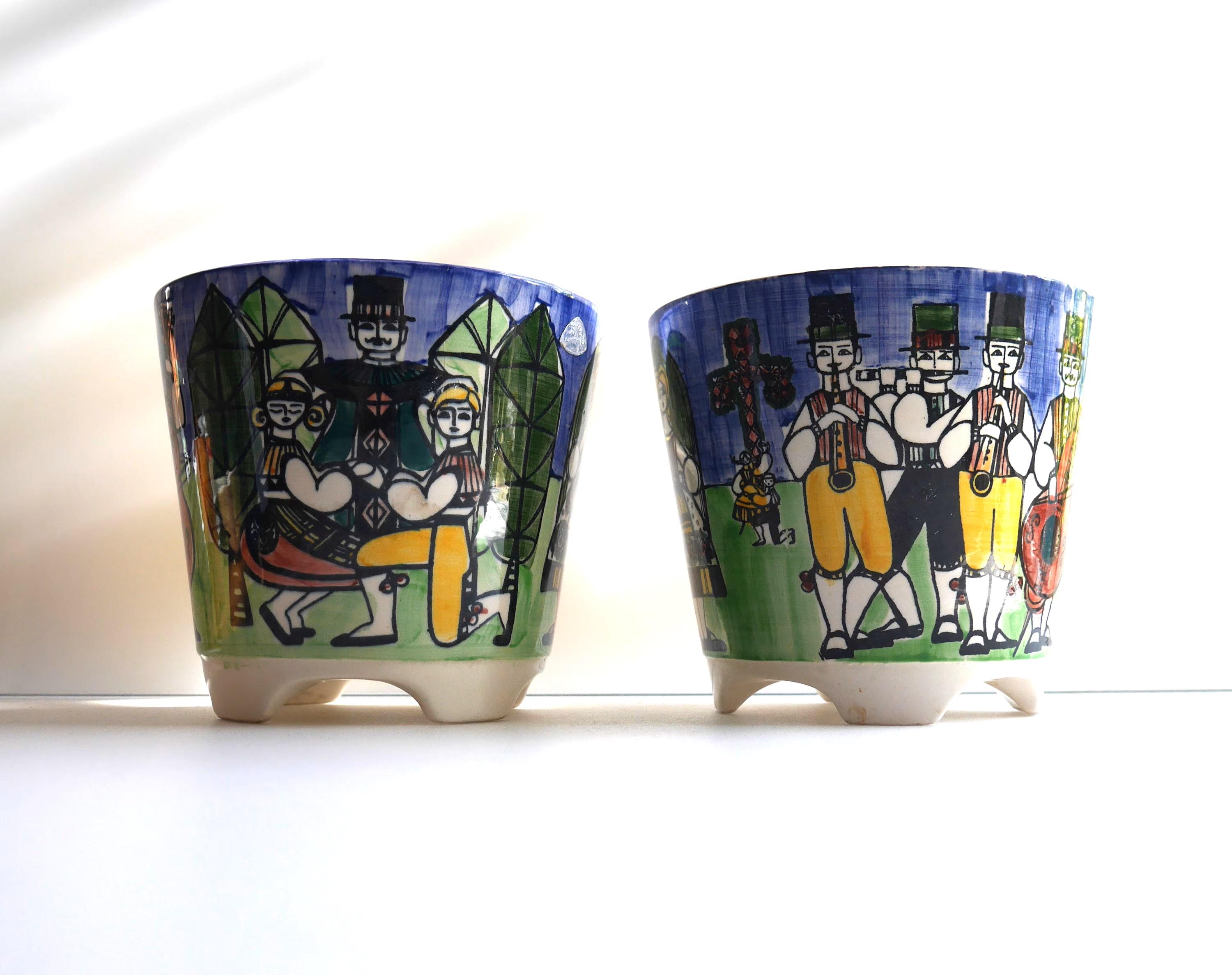 A pair of very nice hand painted vintage porcelain flowerpots made by Anita Nylund for JIE Keramik, Sweden. These pots have fantastic colors depicting a traditional Swedish midsummer dance. There are men and women dancing and playing music in