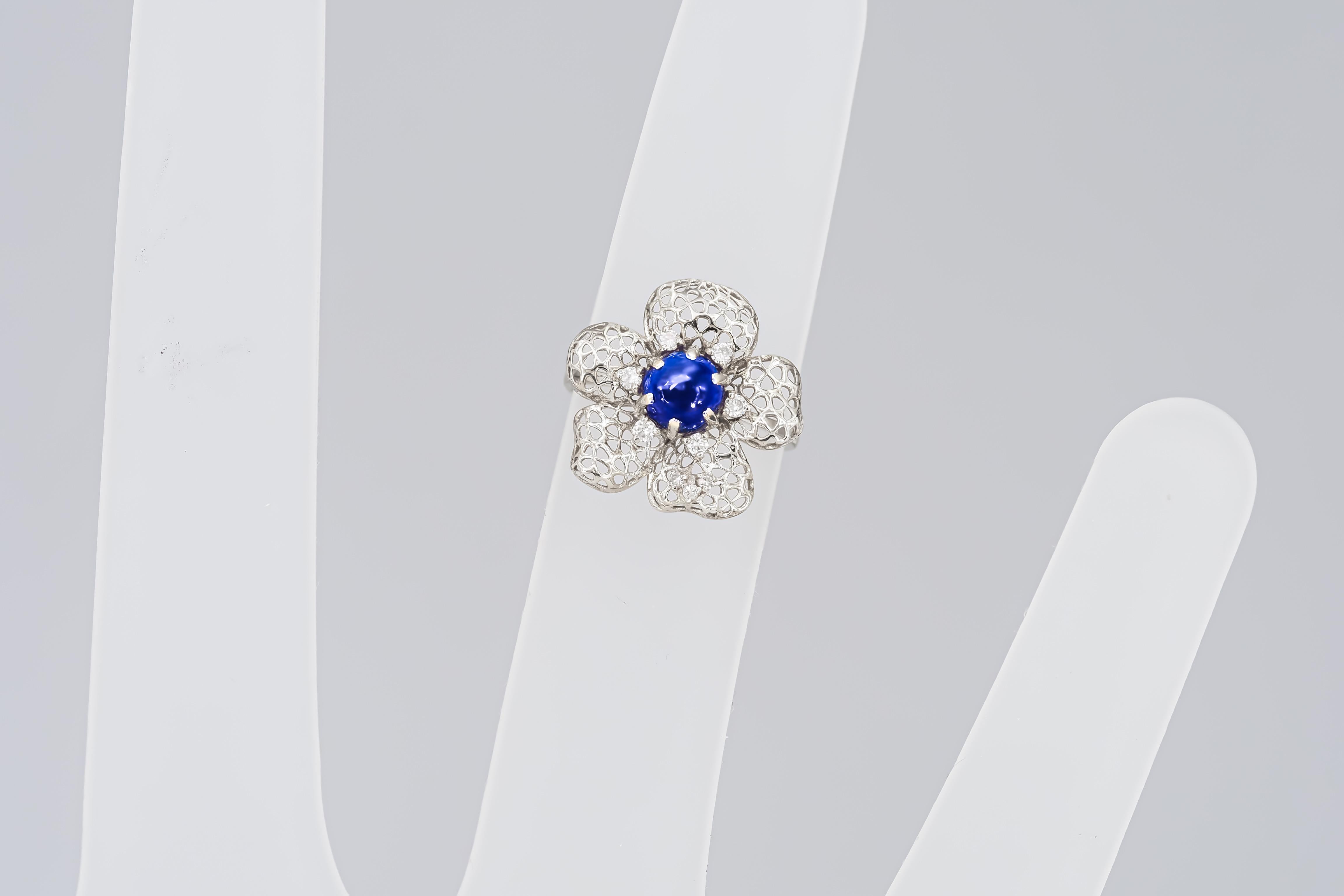 Flower ring with blue sapphire cabohon in 14k gold

Weight: 2.51 g.
Gold - 14 kt gold marked

Central stone: Sapphire
Cut: Round cabochon
Weight: approx 1.30 ct.
Color: Sapphire
Clarity: Transparent with inclusions.
Side stones:  
White topazes: