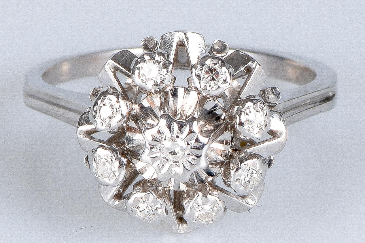 Flower-shaped ring in 18-carat white gold set with a total of 9 Round Brilliant diamonds. One of these diamonds measures 0.017 carats in the centre and 8 surrounding diamonds each measure 0.017 carats, making a total of 0.153 carats. 

With its