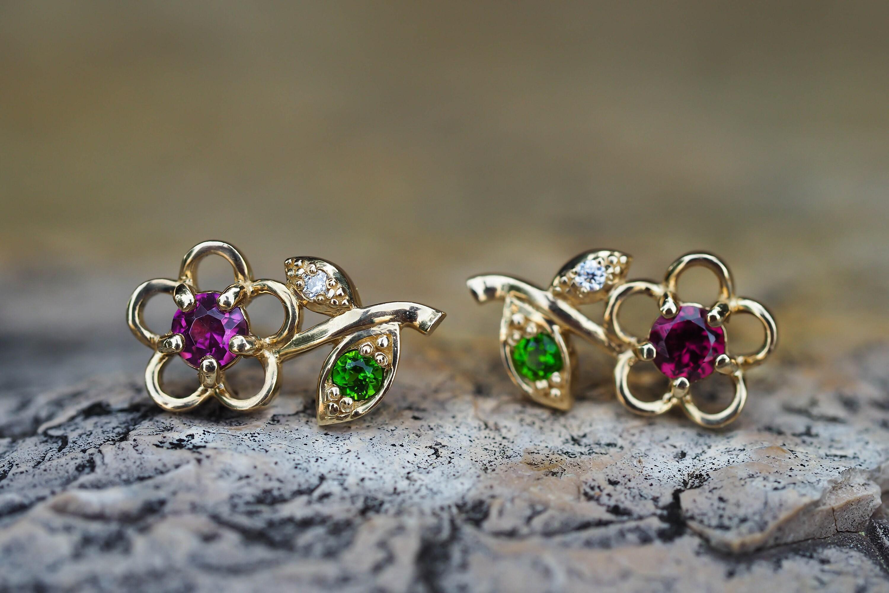 Flower stud earrings in 925 silver.

Metal type: 925 silver
Size: 13 x 6 mm.
Weight: 2.2 g.

Central stones:
Garnets: red and purple color, round cut, clarity good - small inclusions, 0.08x2=0.16 ct total.

Side stones:
Tsavorites: 2 pieces, green