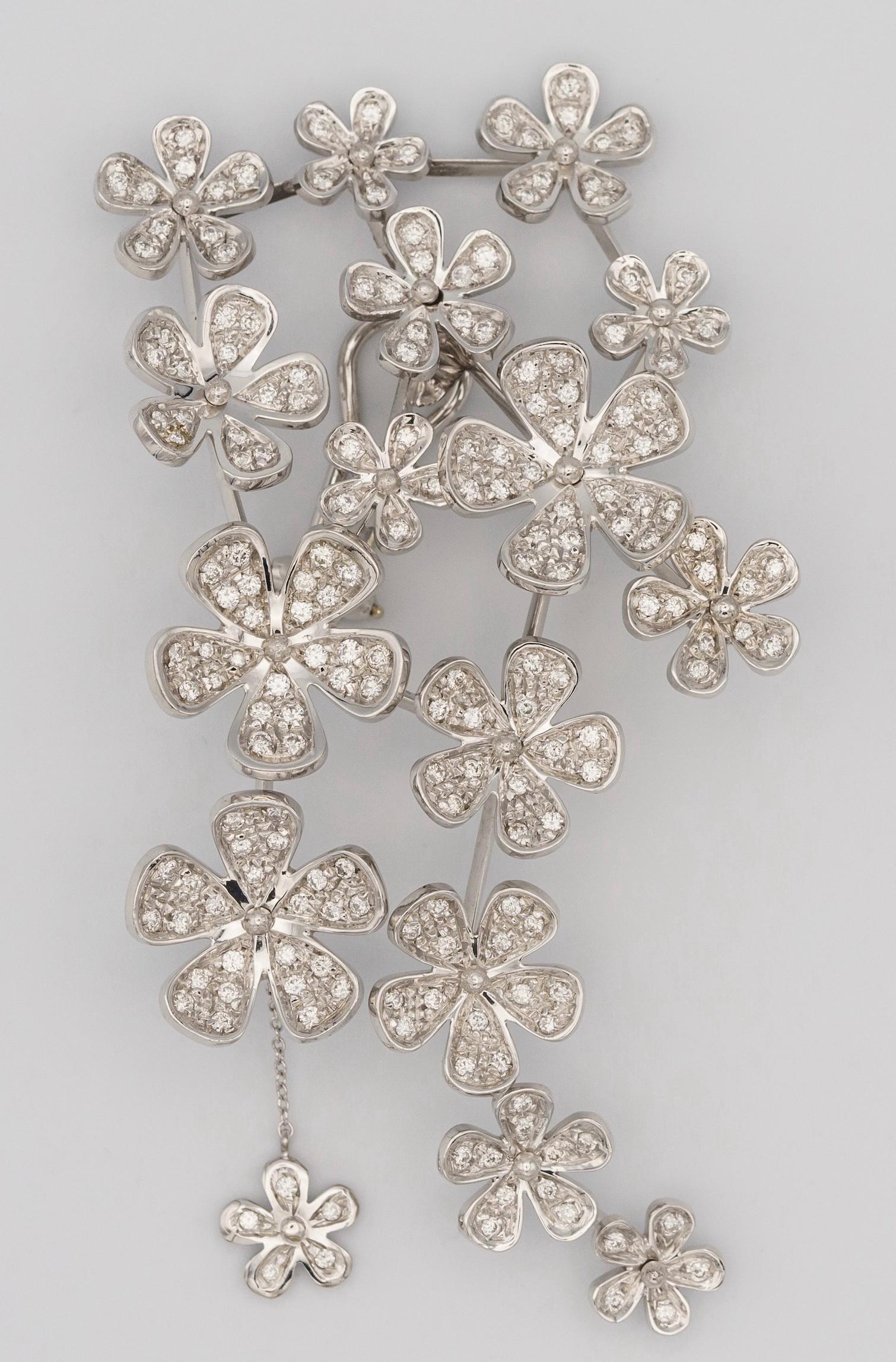 Cette magnifique paire de boucles d'oreilles fleurs en or blanc pavées d'environ 10 carats de diamants présente un design qui les rend uniques.
Certains motifs sont en relief et tournent pour donner du mouvement au dessin. Toujours dans cette