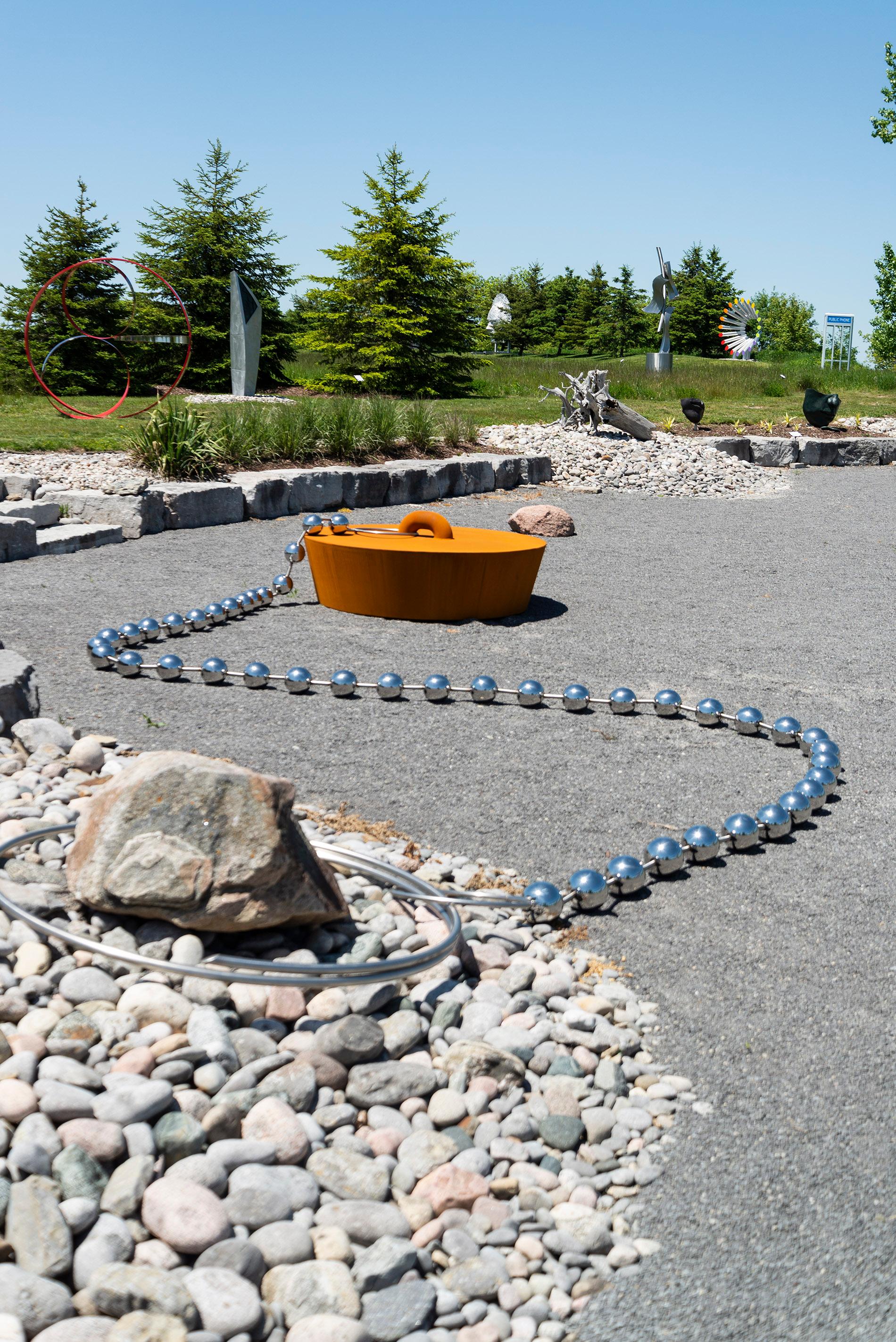 This fun and fanciful large outdoor pop art sculpture is by Floyd Elzinga. This piece is a massive corten steel drain plug attached to a long polished stainless chain. The form is obviously inspired by the old-fashioned rubber sink/tub stoppers. The