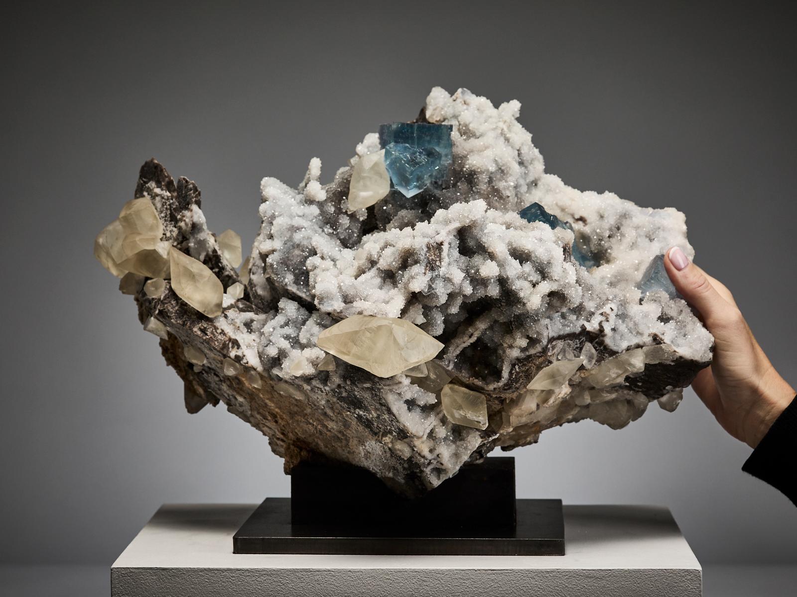 This exceptional specimen from La Viesca mine, La Collada, Asturias, Spain features sharp purple and blue fluorite cubes beautifully set on a bed of white quartz crystals. Scattered across the matrix are elegant, creamy, double-terminated calcite