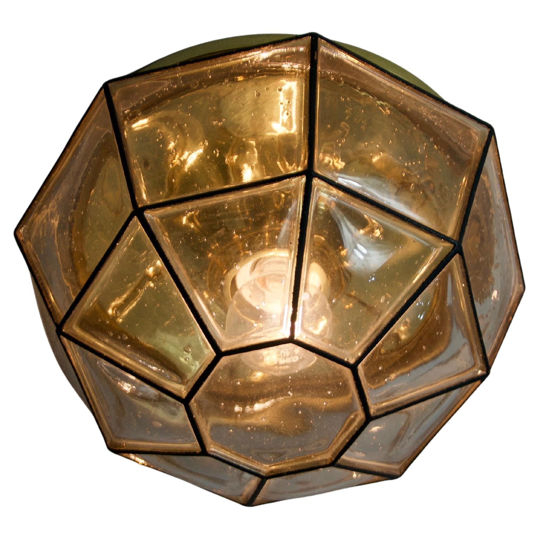 Ce superbe plafonnier en laiton de Limburg datant des années 1960 incarne l'élégance intemporelle et l'artisanat de haute qualité. Son design géométrique, composé de panneaux de verre structurés aux teintes chaudes et dorées, crée un jeu d'ombre et