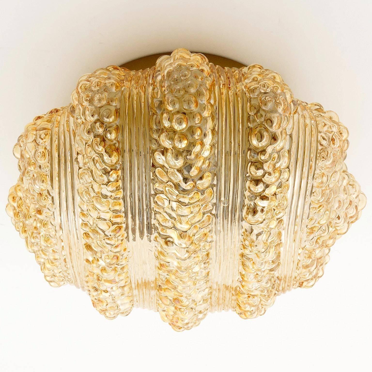 One of three fantastic textured glass light fixtures, manufactured in Germany in midcentury, circa 1970 (late 1960s or early 1970s).
An amber, yellow, orange, honey, champagne toned textured bubble glass is mounted on a golden or brass tone painted