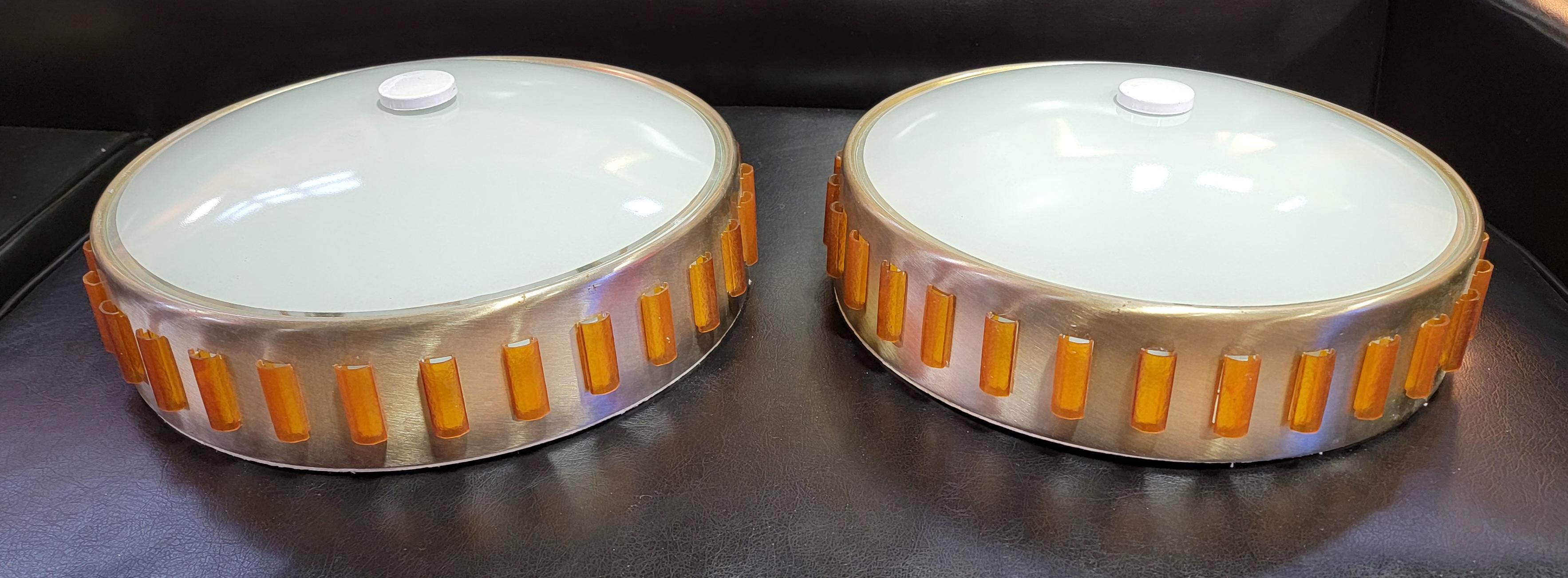 A pair of Mid-Century Modern flush mount ceiling fixtures with a space ship design. Metal frames, glass domed shades with amber colored plastic vents. Excellent original condition with original wiring working as intended. Each fixture holds 3 light