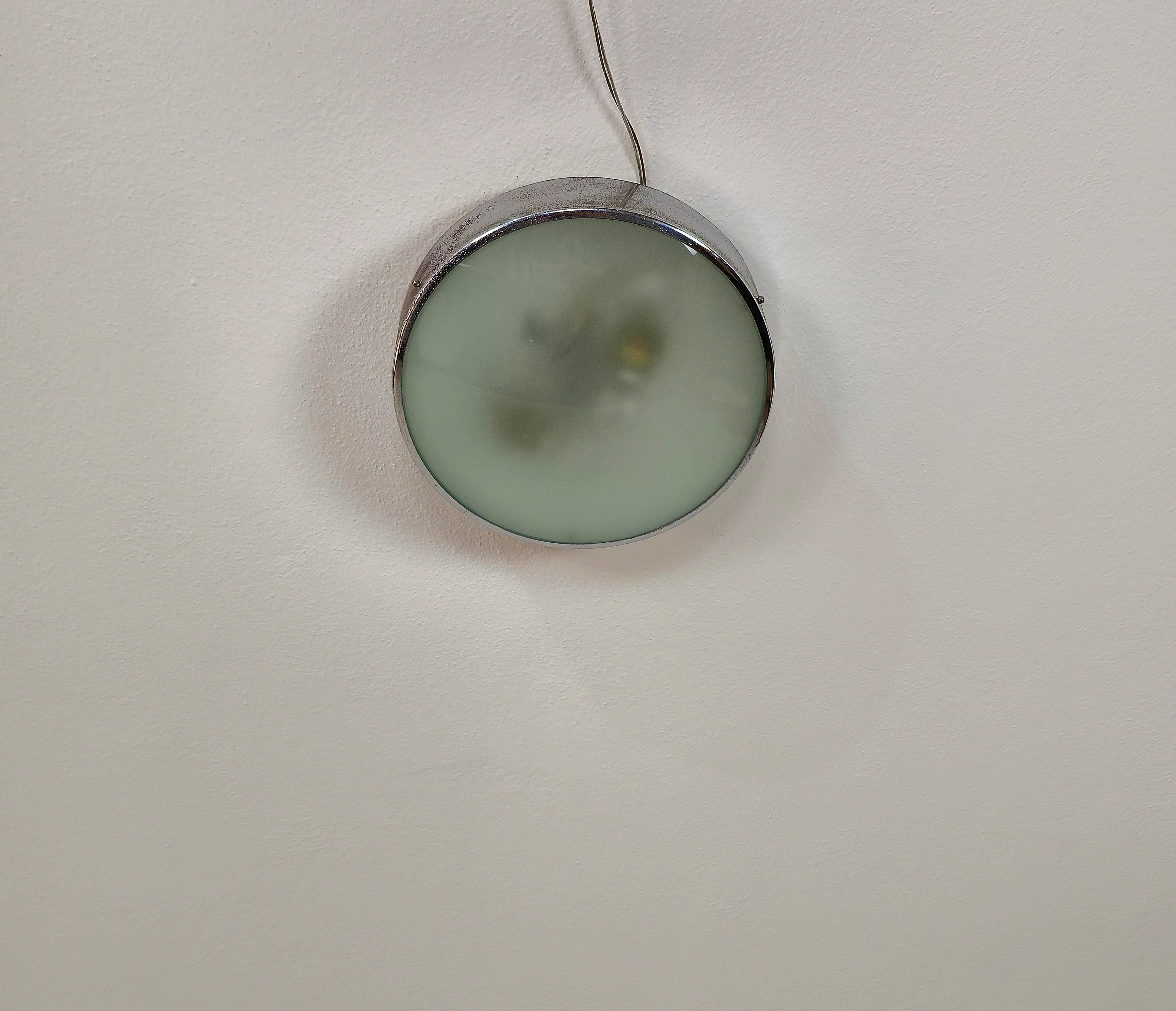 Plafonnier/applique produit dans les années 60 dans le style de Fontana Arte.
Le plafonnier a une structure avec 2 lampes E27 en métal émaillé avec une bordure en métal chromé qui soutiennent ensemble un verre opaque concave dans la nuance du vert