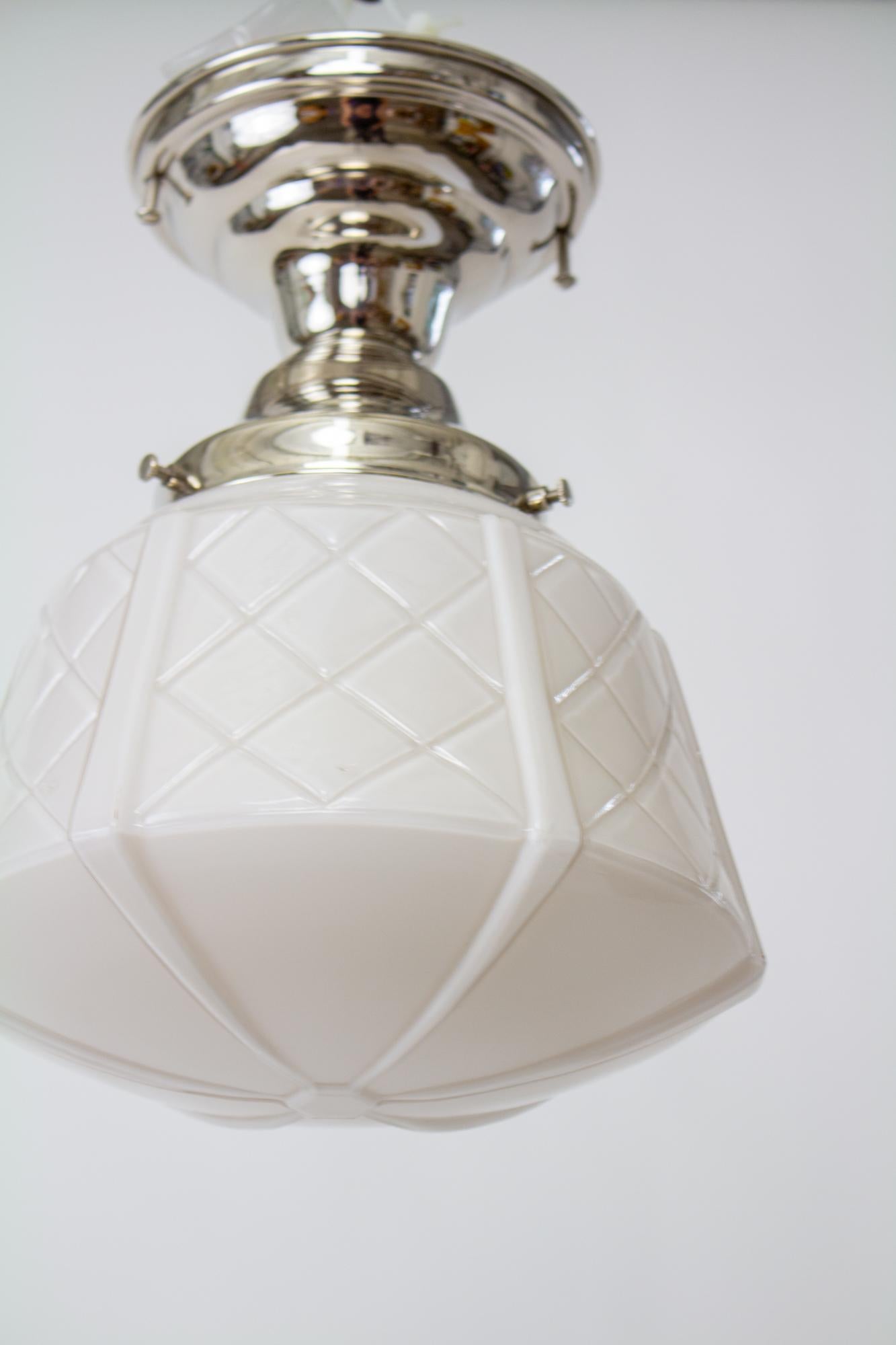 Flush mounted polished nickel Art Deco fixture with white cased glass. The glass shade has a criss-crossed shape and tapers to a wider shape at the bottom. C. 1930, American. The fixture is a new replacement, in polished nickel. It has a single