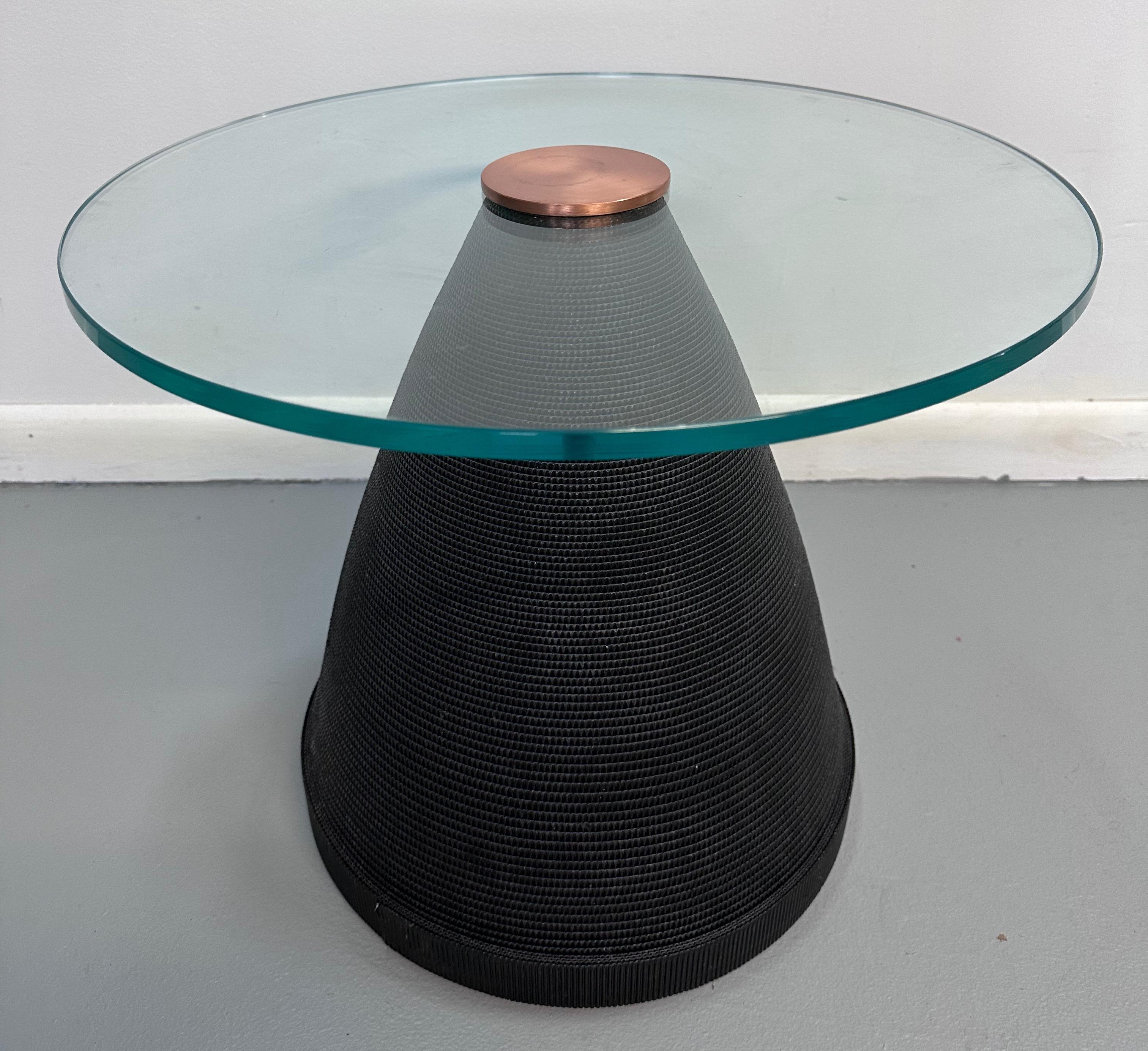 Magnifique table d'appoint post-moderne construite en carton ondulé noir enveloppé dans une forme conique, surmontée d'un plateau en verre de 20 pouces de diamètre et coiffée d'un joli disque en laiton qui verrouille la table en place. 

La table