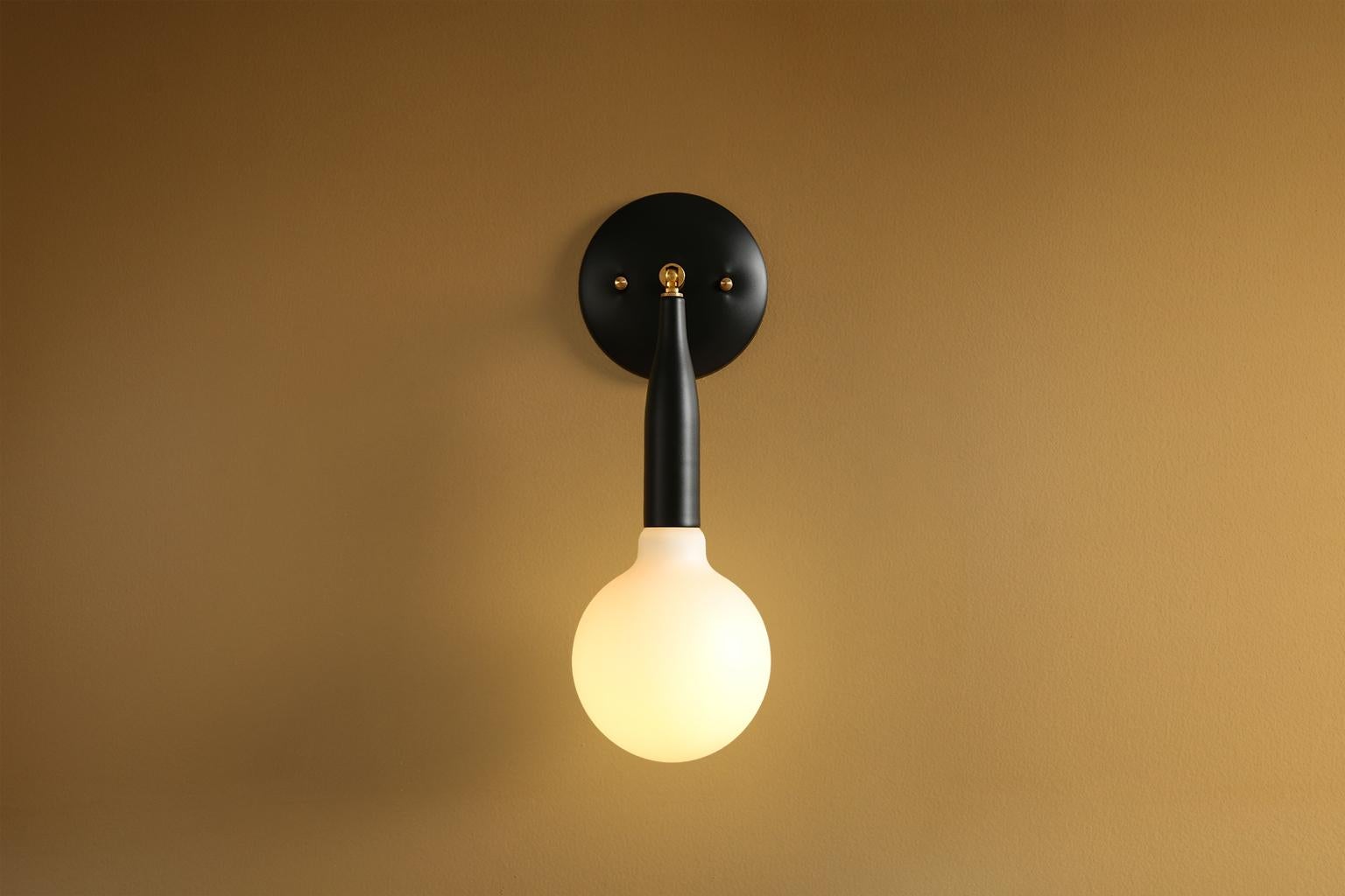 Un aplique de pared minimalista, este accesorio de iluminación contemporáneo se ajusta hacia arriba y hacia abajo y de lado a lado. La flauta hecha a medida está perfectamente proporcionada para reflejar las curvas de una copa de champán. Los