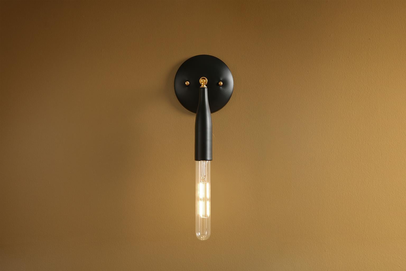 A minimalist wall sconce, this contemporary light fixture adjusts up and down and side to side. The custom-made flute is perfectly proportioned to echo the curves of a champagne glass. Powder coated colors, metallic details, and exposed bulbs give a