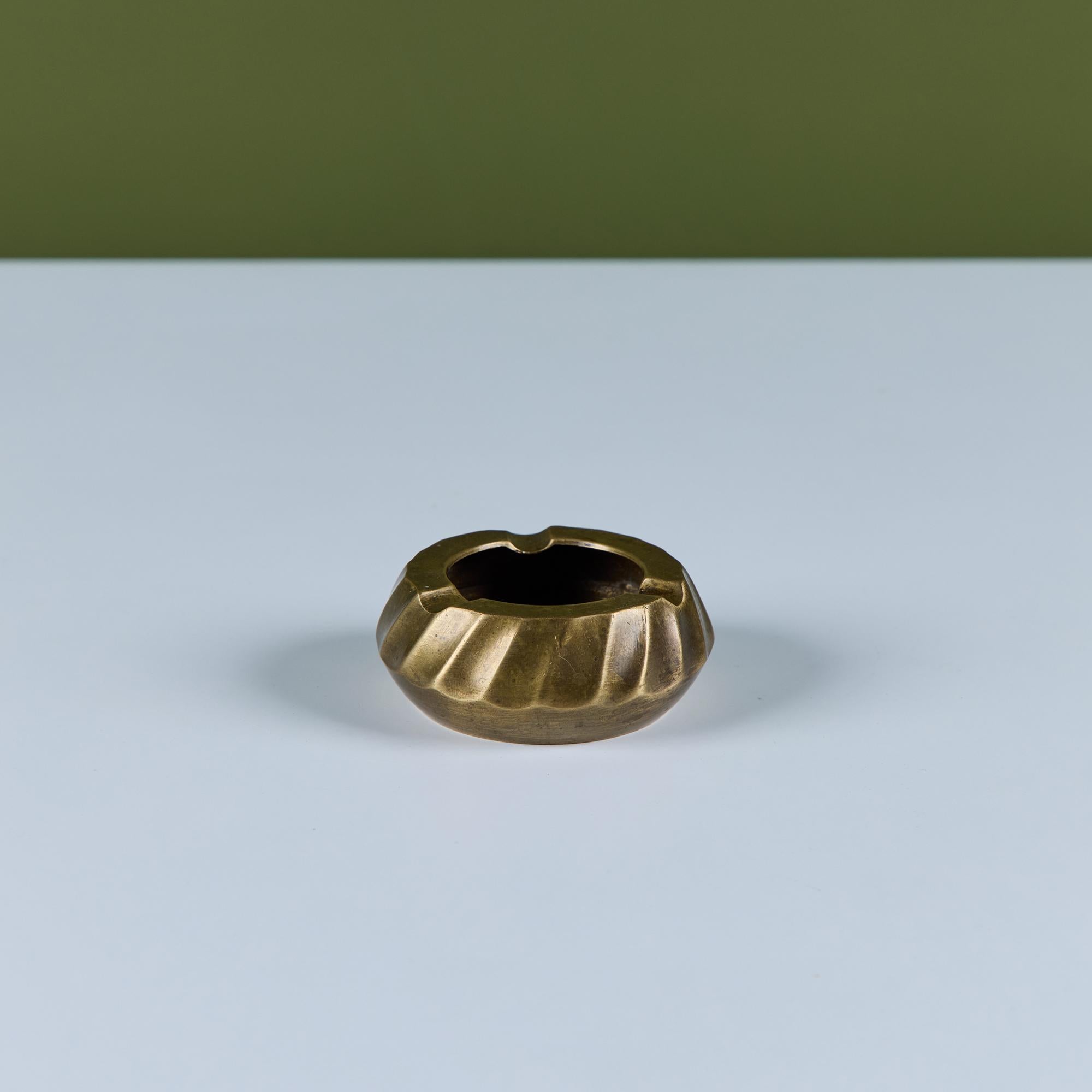 Der zierliche Aschenbecher aus geriffeltem Messing hat eine runde Form mit einem tiefen Schacht und drei Zigarettenkerben.

Abmessungen
3
