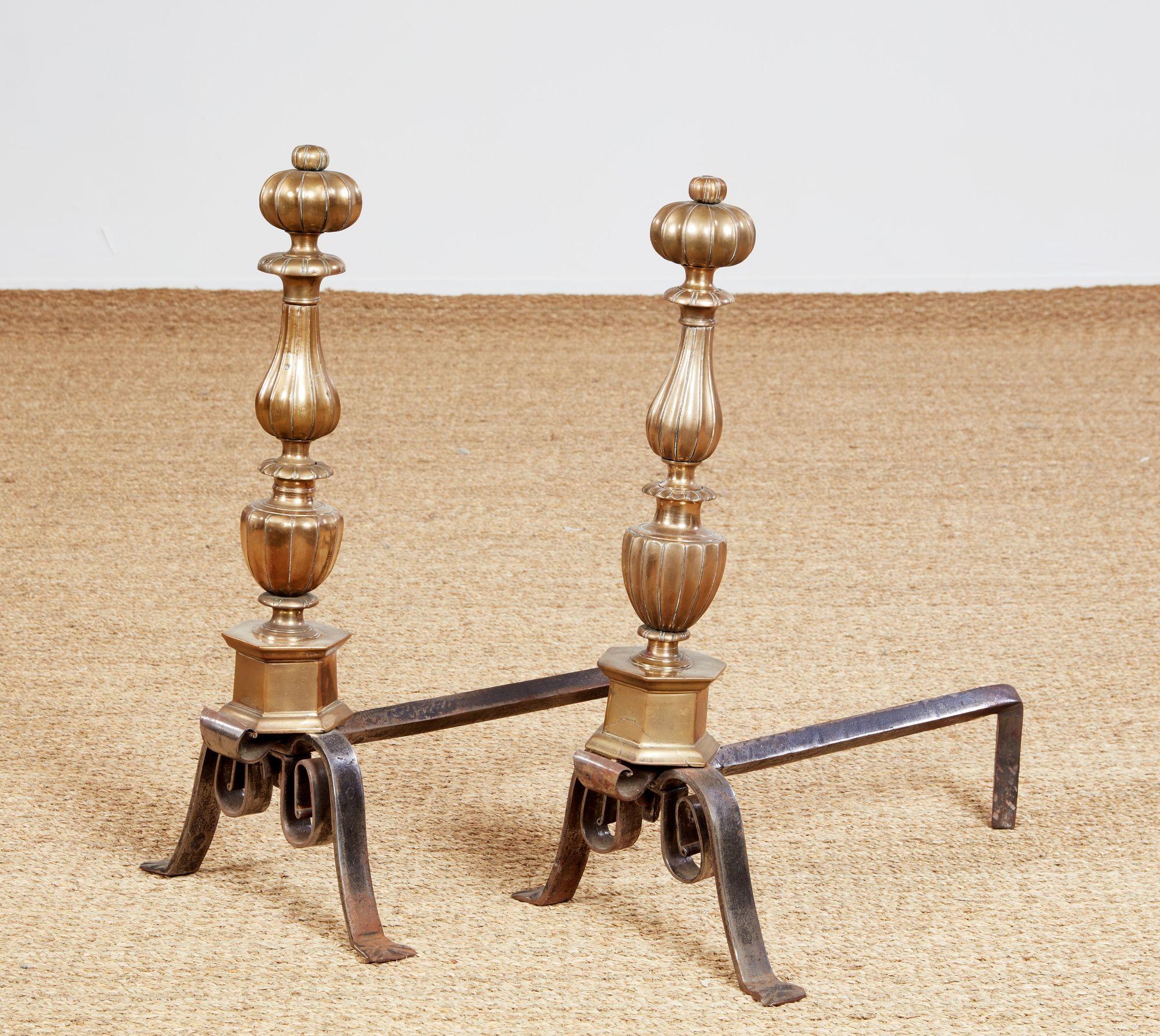 A pair of shapely bronze andirons of fluted baluster form with narrow waists and ring turnings having a mellow bronze patina. The shafts on hexagonal base with forged arched and coiled steel legs. Topped with double onion finials. Distinguished