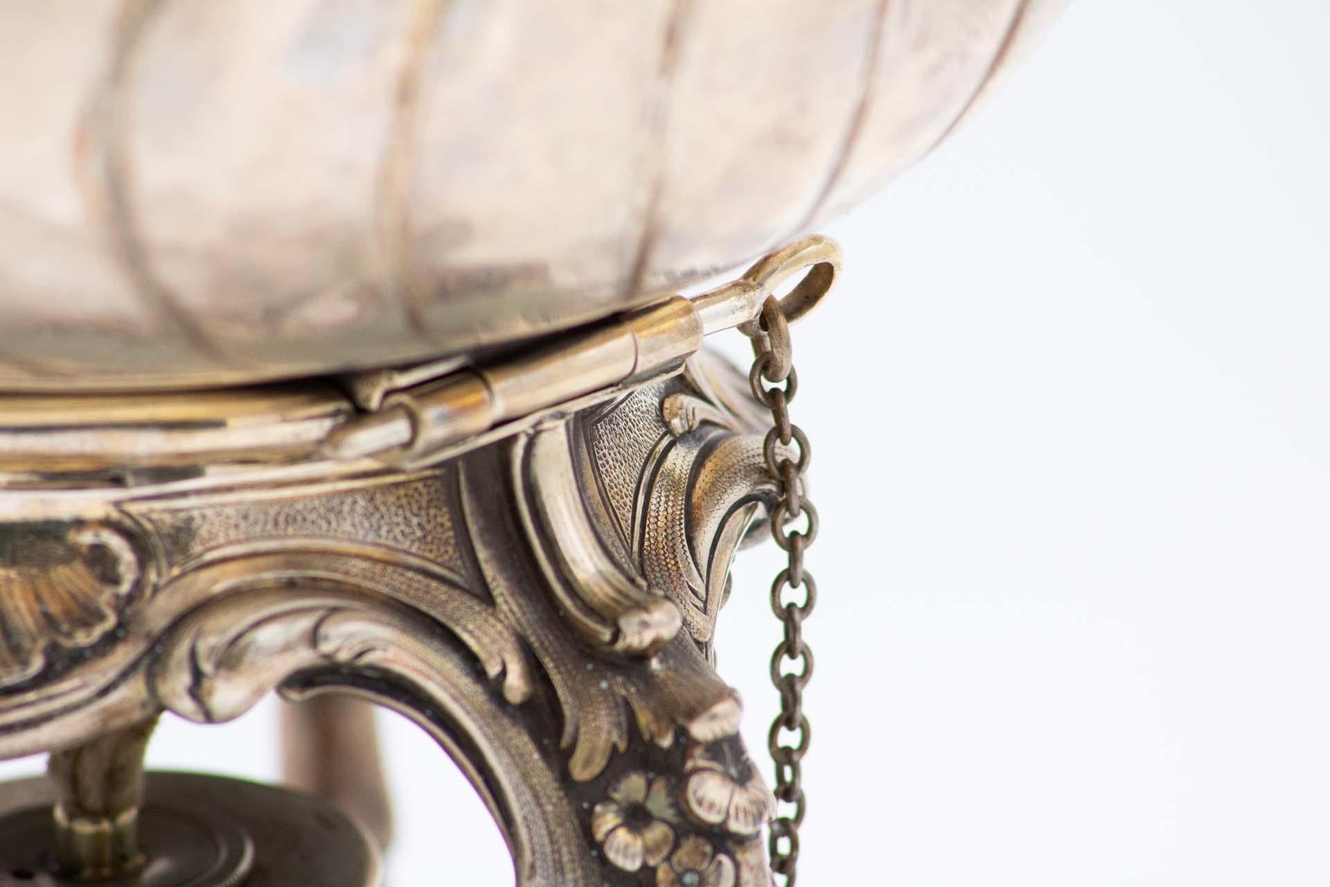 Description : Bouilloire en argent gommé à trois pieds surélevés et révélés par des motifs floraux, bouton en forme de cauris sur le couvercle, poignée mobile et lampe chauffante. Métal : Argent. Origine : Allemand. Marque : Inconnu. Poids : 1996,57