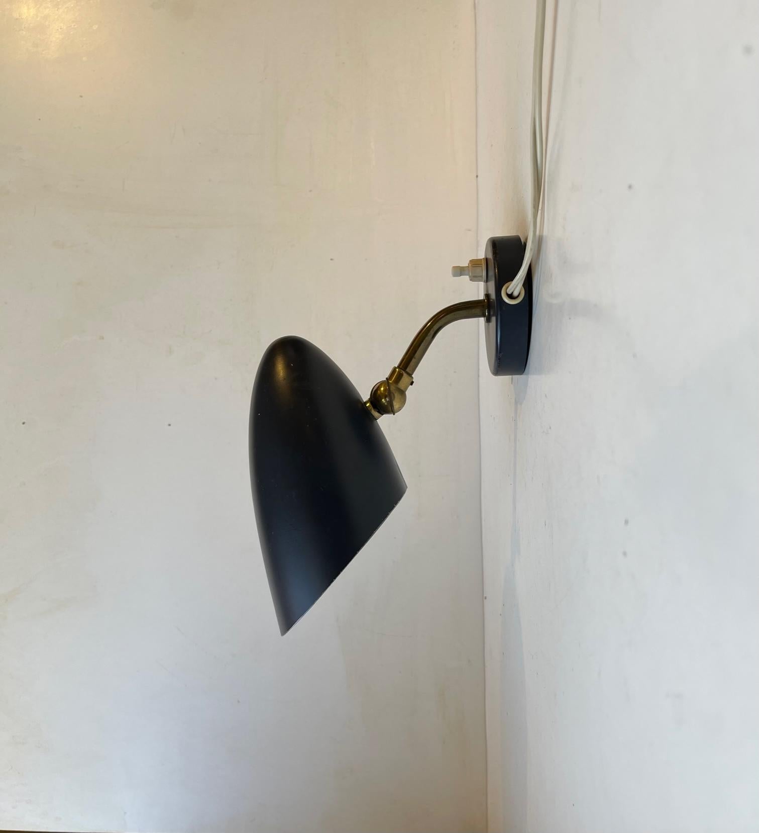 This small stylish matte black wall light was manufactured by Fog & Mørup in Denmark during the 1940s. The piece features an adjustable patinated brass rod that allows the user to direct light to the desired location. Reminiscent in style to pieces