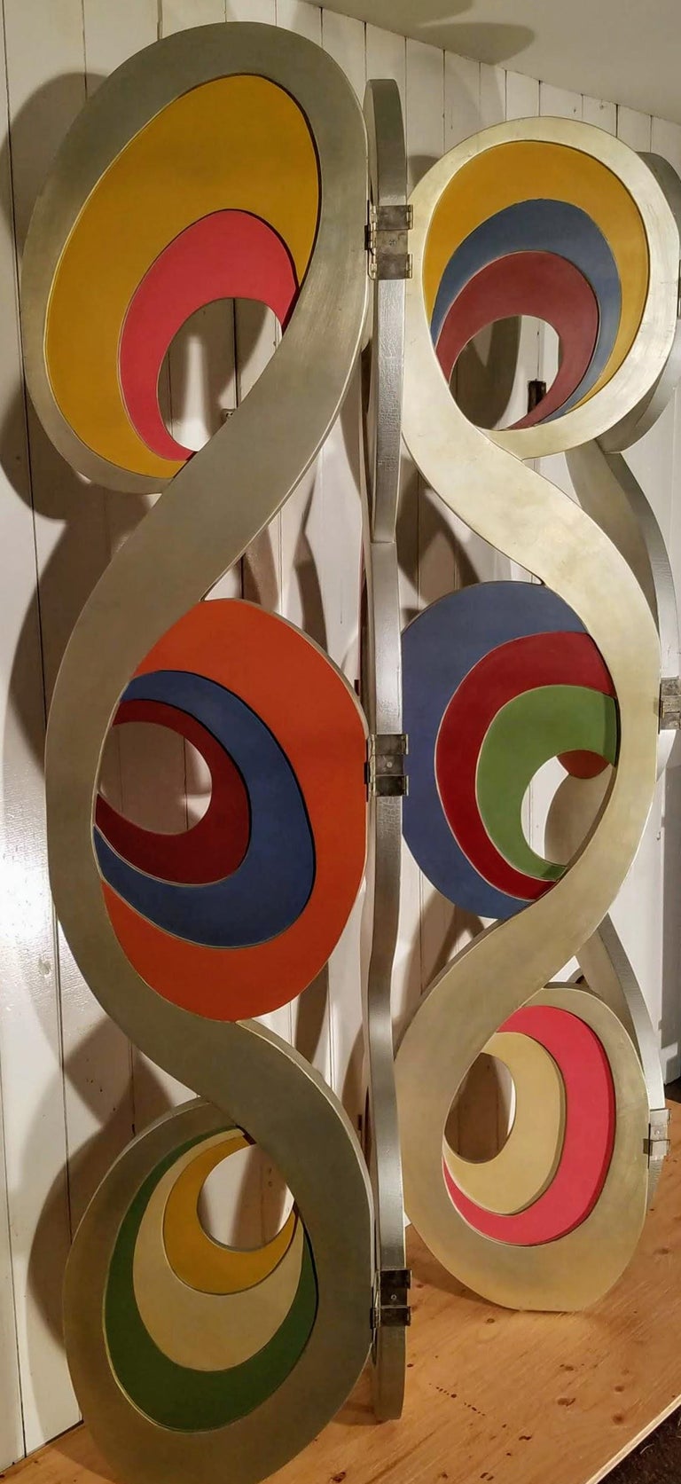 A 4-panel aluminum-leafed folding floor screen from the 1980s possibly Italian or French.

Each panel is its own individual design constructed of six cut-out sheets of wood, laminated and sculpted into arabesque curls.

The panels are connected