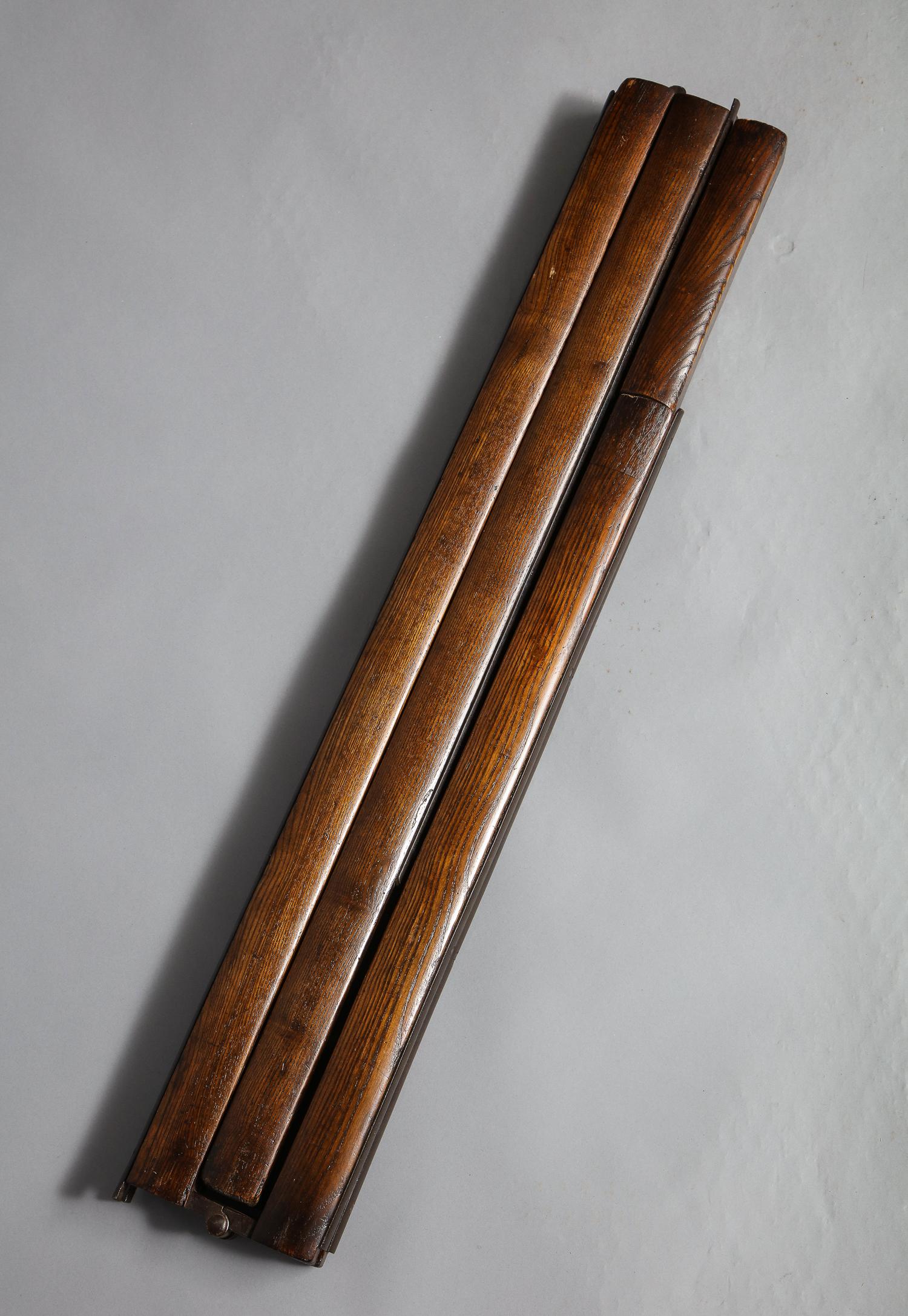 A library ladder of polished wood uprights with black iron rungs and iron hinge fittings that folds first into a pole and then further into to a three foot unit.