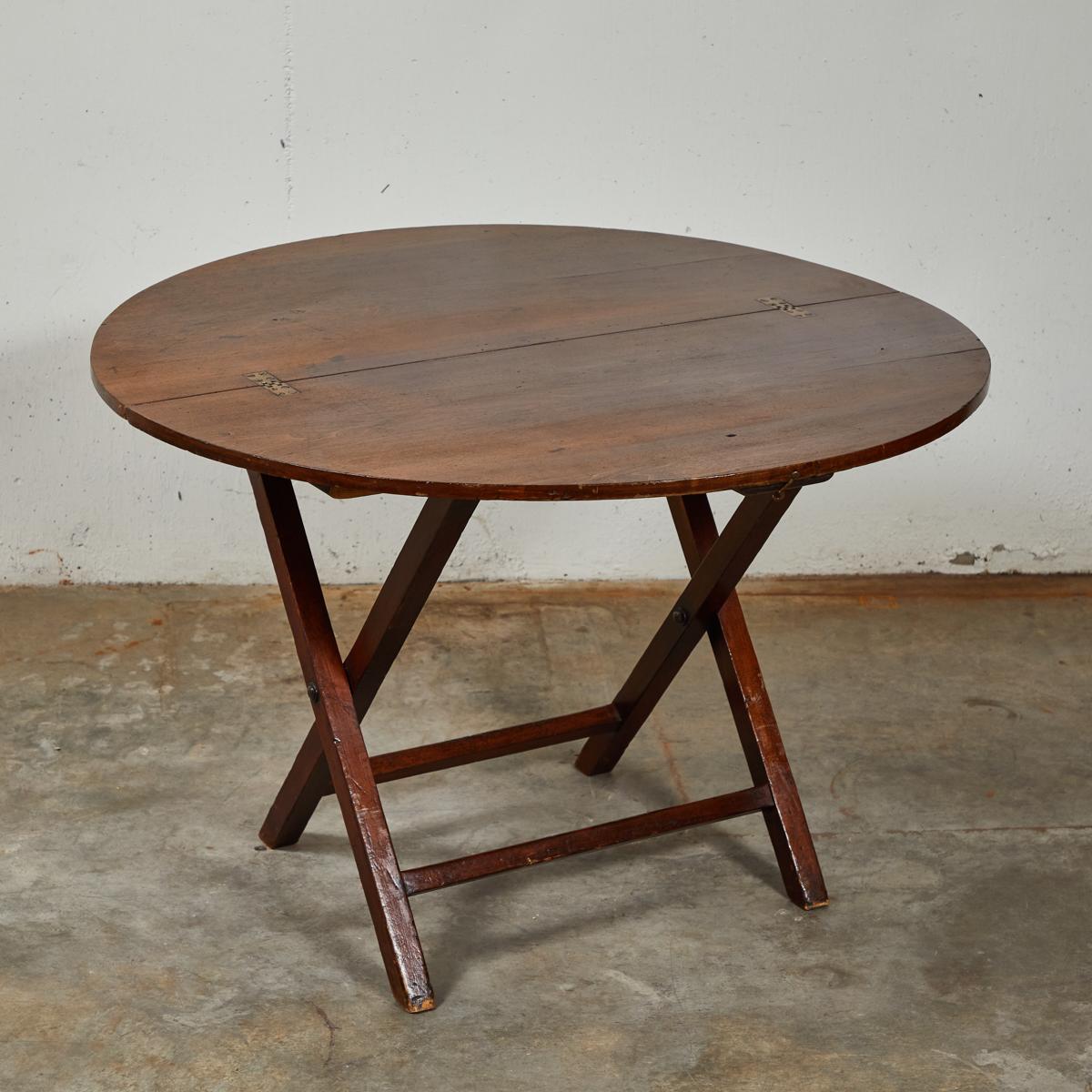 19th Century English mahogany folding coaching / campaign table; the round mahogany top, supported on X-shaped supports, with turned stretchers. Great use for a small dining table, coffee table, game table or side table.