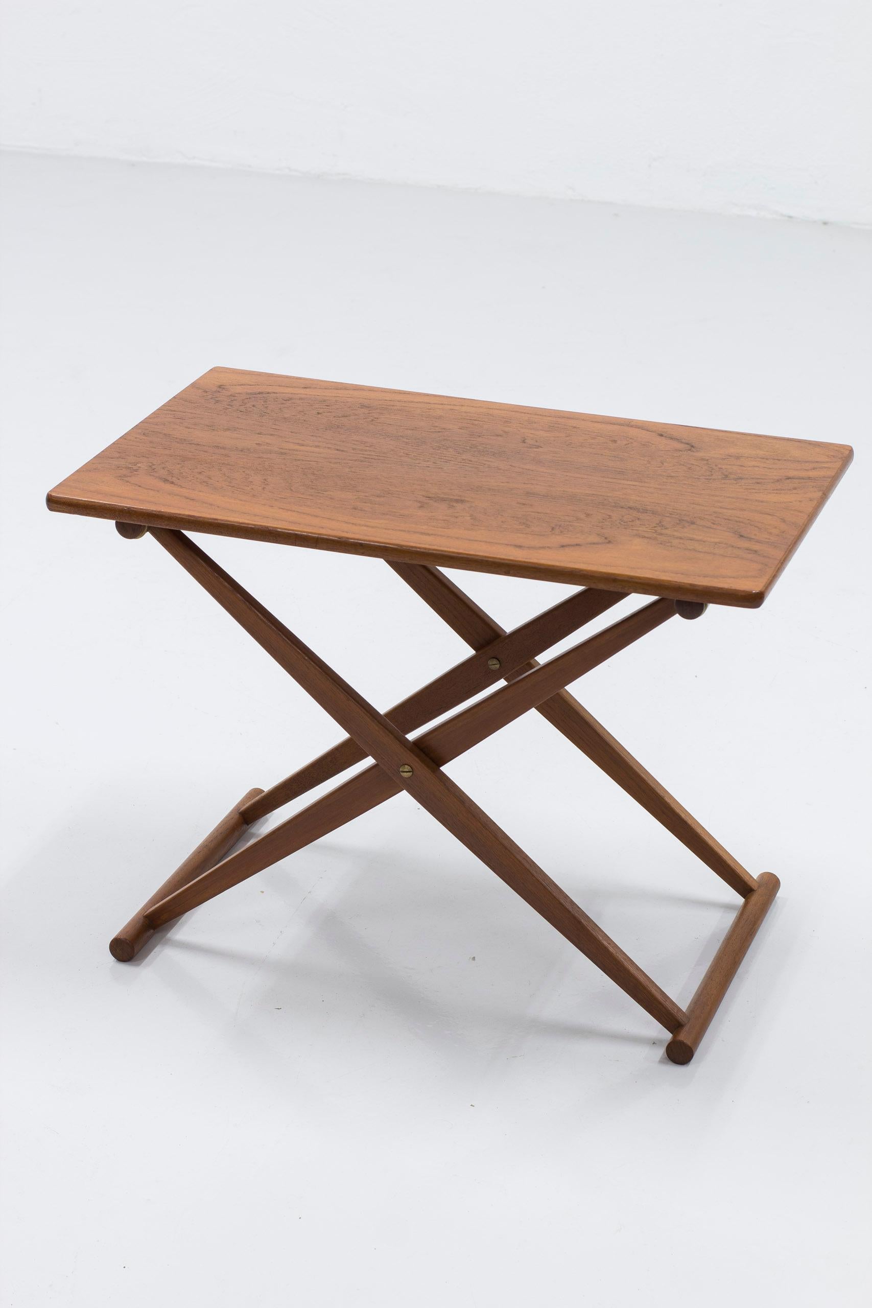 Folding side table designed by Knud Andersen. Produced by Cabinetmaker J.C.A. Andersen in Denmark. Made during the 1950s. Solid teak base with brass details and table top in teak. The table folds together easily for storage. Very good vintage