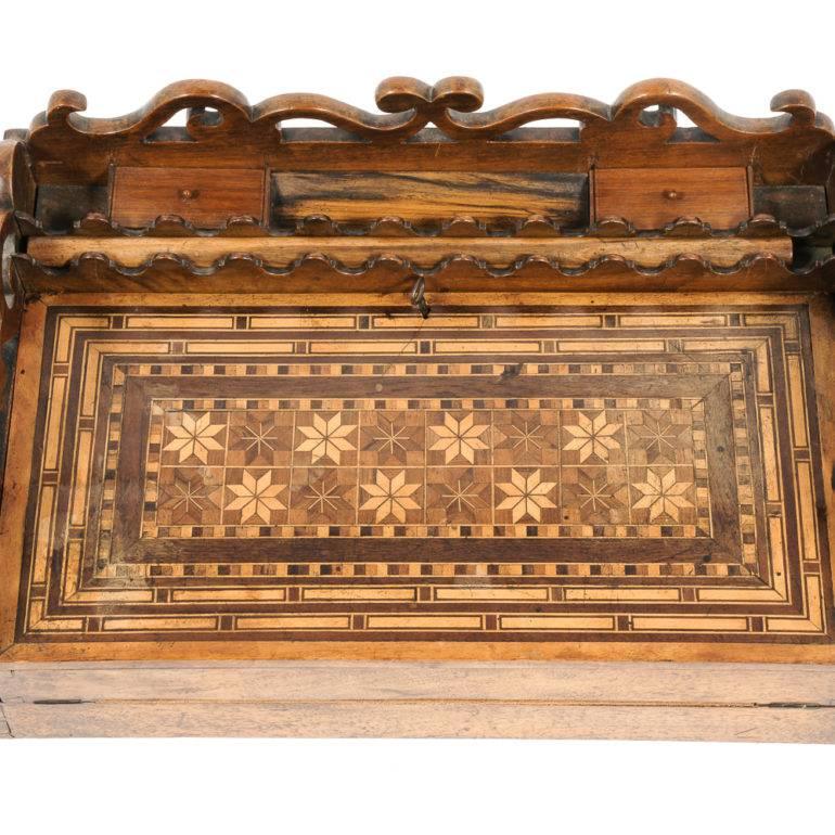 An unusual traveller’s desk with pierced gallery surround enclosing lidded compartments, and slot for a pen, the marquetry top opening to reveal fitted drawers, as well as a hardwood ‘dowel’ in its own slot- likely used to roll over blotting