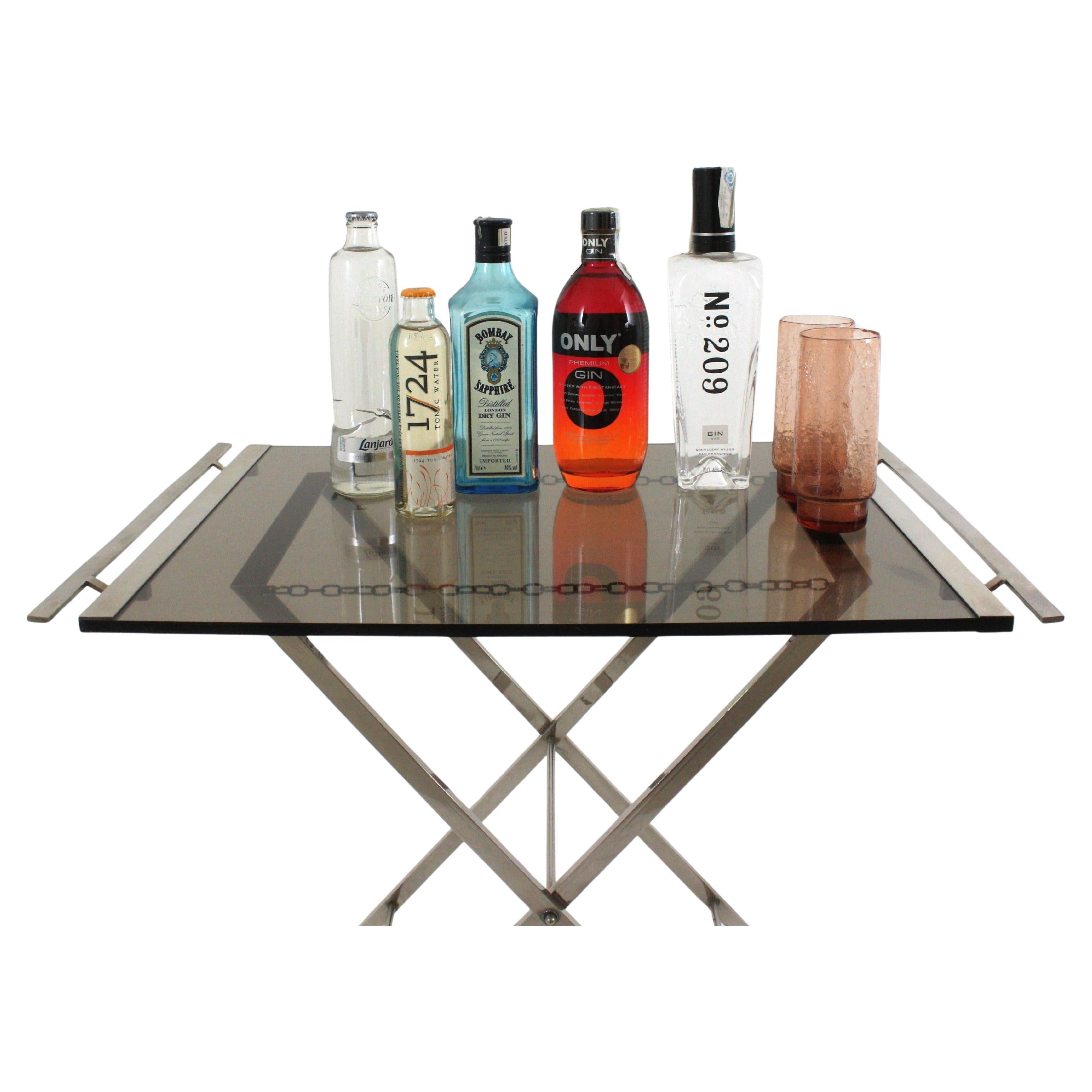 Table pliante en lucite et acier chromé, France, années 1970.
Cette table à cocktails ou table à boissons se compose d'un pied pliant en X en acier chromé et d'un plateau de service constitué d'une épaisse feuille de lucite fumée avec des poignées