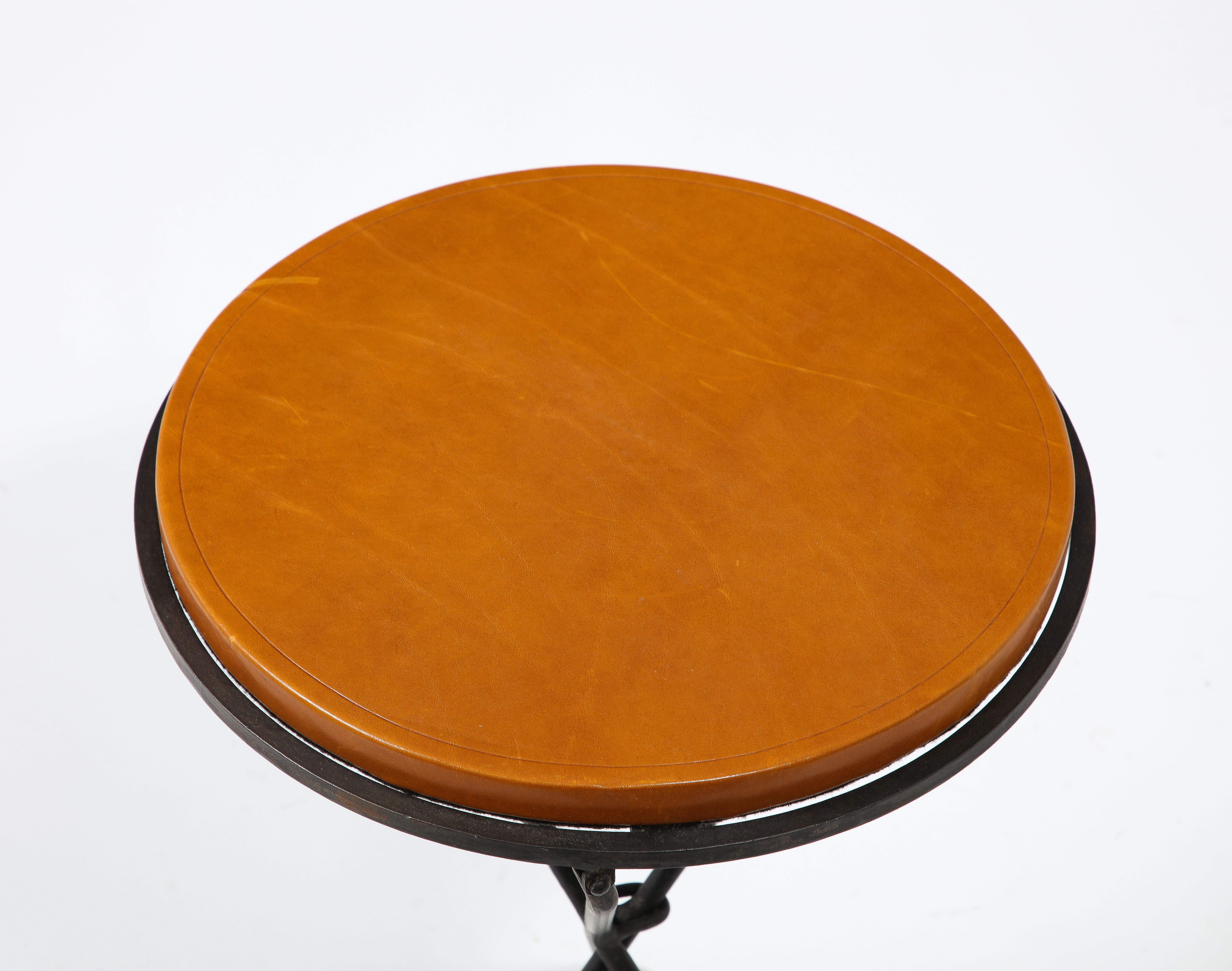 A folding wrought iron table with a leather top, the hanging ring is meant to be used to hang the table flat when not in use.