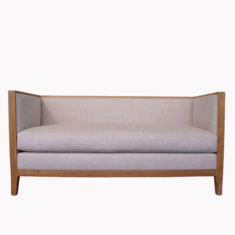 French style settee interpreted from a classic Jean-Michel Frank design. Tight back and sides on interior with loose seat cushion shown in light cerused oak and natural linen. Custom finishes available also available in ebonized walnut and medium