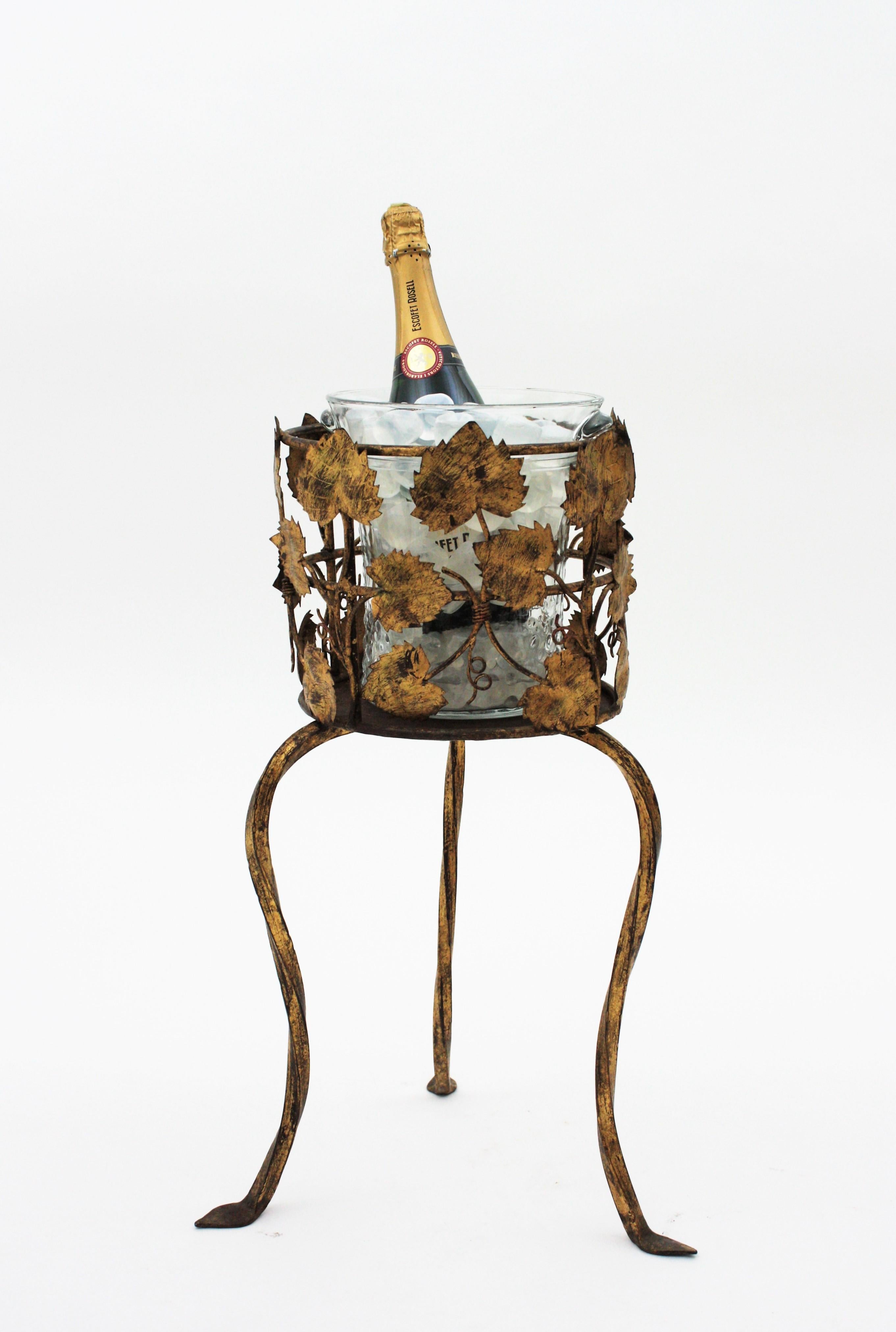 One of a kind foliage gilt iron tripod stand with pressed glass ice bucket, Spain, 1940s
This iron ice bucket serving stand is all made by hand. The handwrought iron stand has a leafed richly adorned top showing gilt iron vine leaves thorough. It