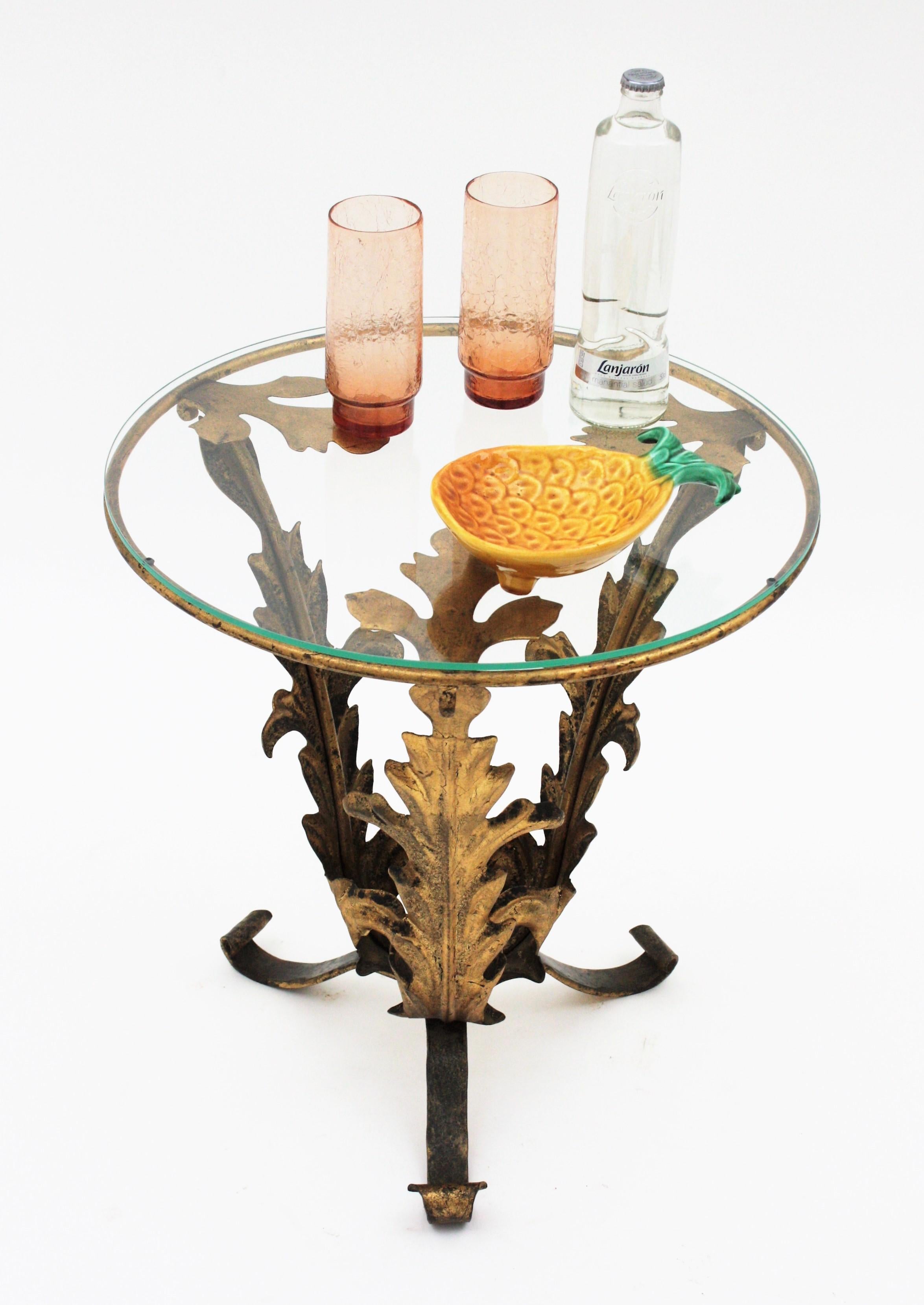 Spanish Drinks Table or Side Table with Foliage Design, Spain, 1940s
Materials: Iron, Gold Leaf, Glass
Stunning Hollywood Regency gilt iron  tripod table with foliage base and glass top.
This beautiful hand wrought iron round table stands up on