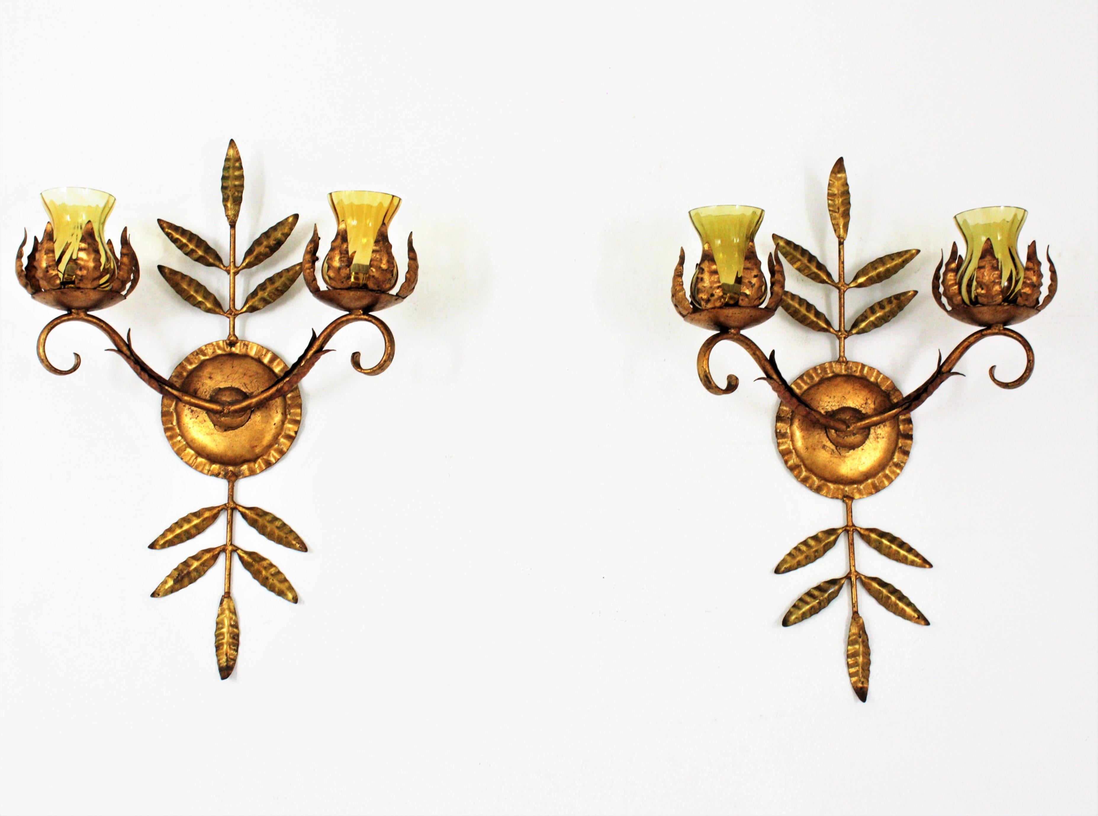 Elegant pair of two-arm gilt iron foliage wall lights with amber glass shades. Spain, 1940s
The backplate has a design of leaves holding two arms with one light each. Each arm has a leafed top and supports the bulb holder with an amber glass