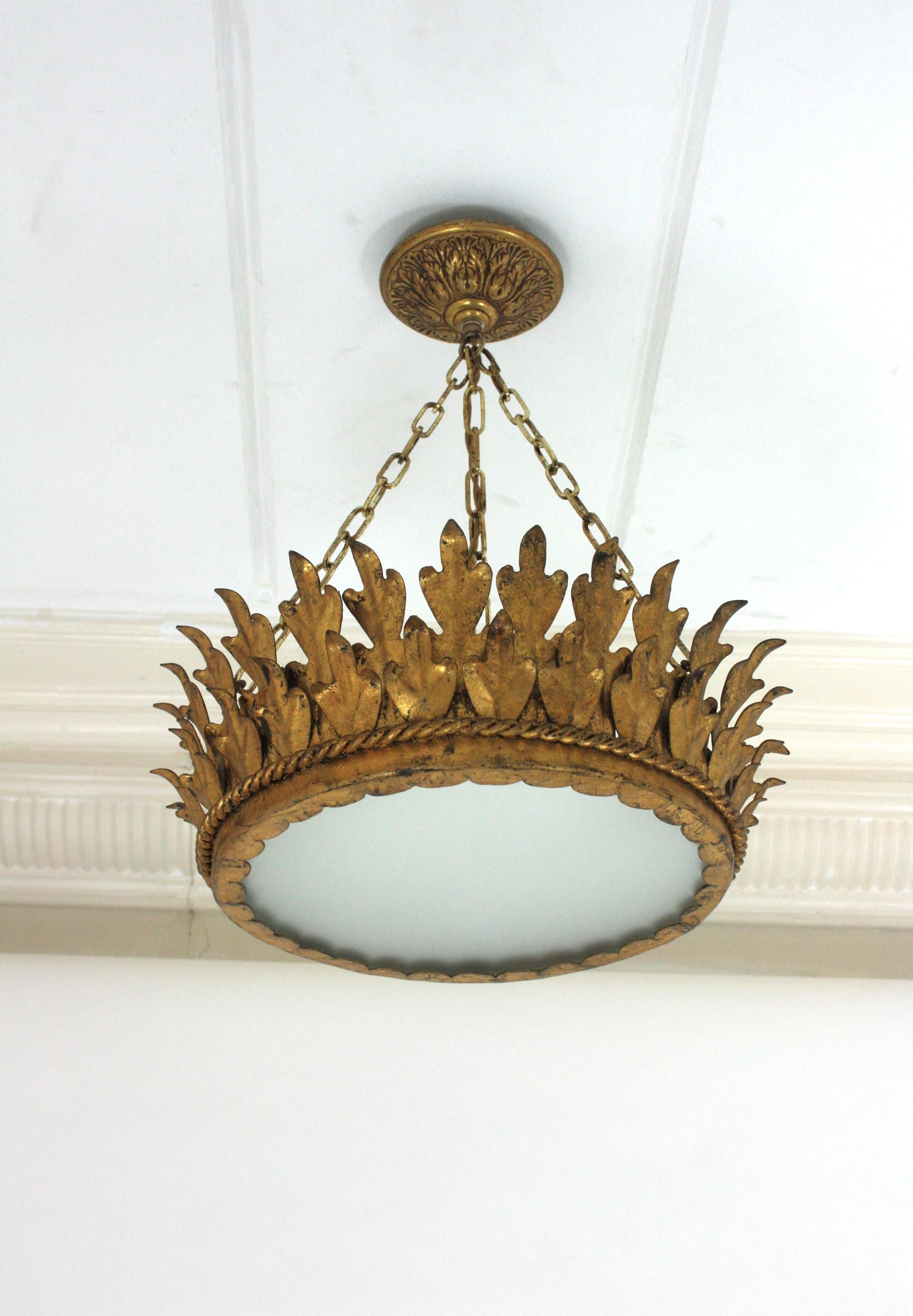 Double Layered Foliage Crown Shaped Ceiling Light Fixture / Pendant, Spain, 1940s.
This spanish pendant features two layers of leaves hand-crafted in gilt iron surrounding a central frosted glass diffuser creating a sunburst or crown shape.