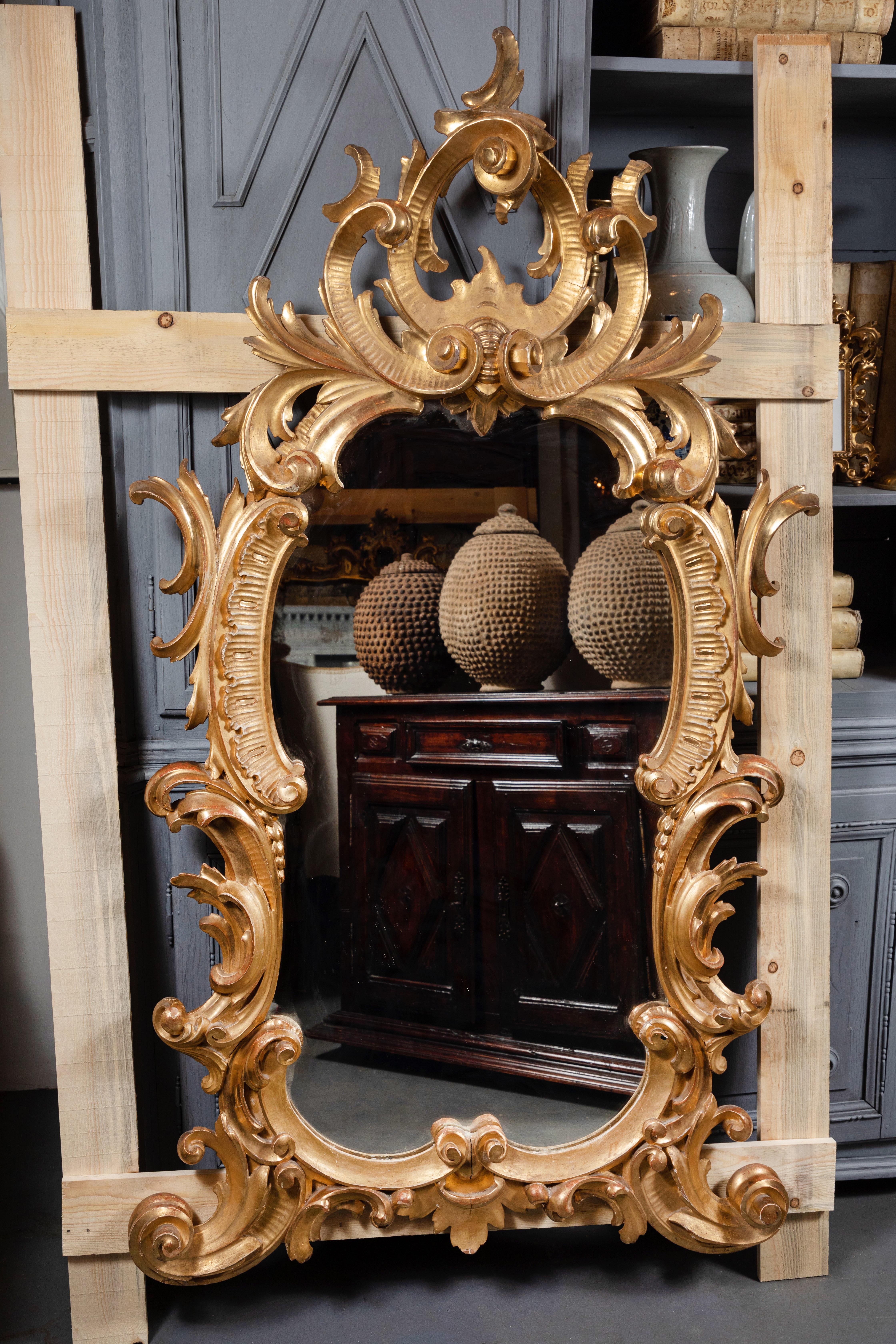 Large, circa 1880, hand carved, gessoed and 22k gold gilded scrolling frame inset with original glass mirror. Surmounted by a dramatic, pierced, foliate crown. From central Italy.