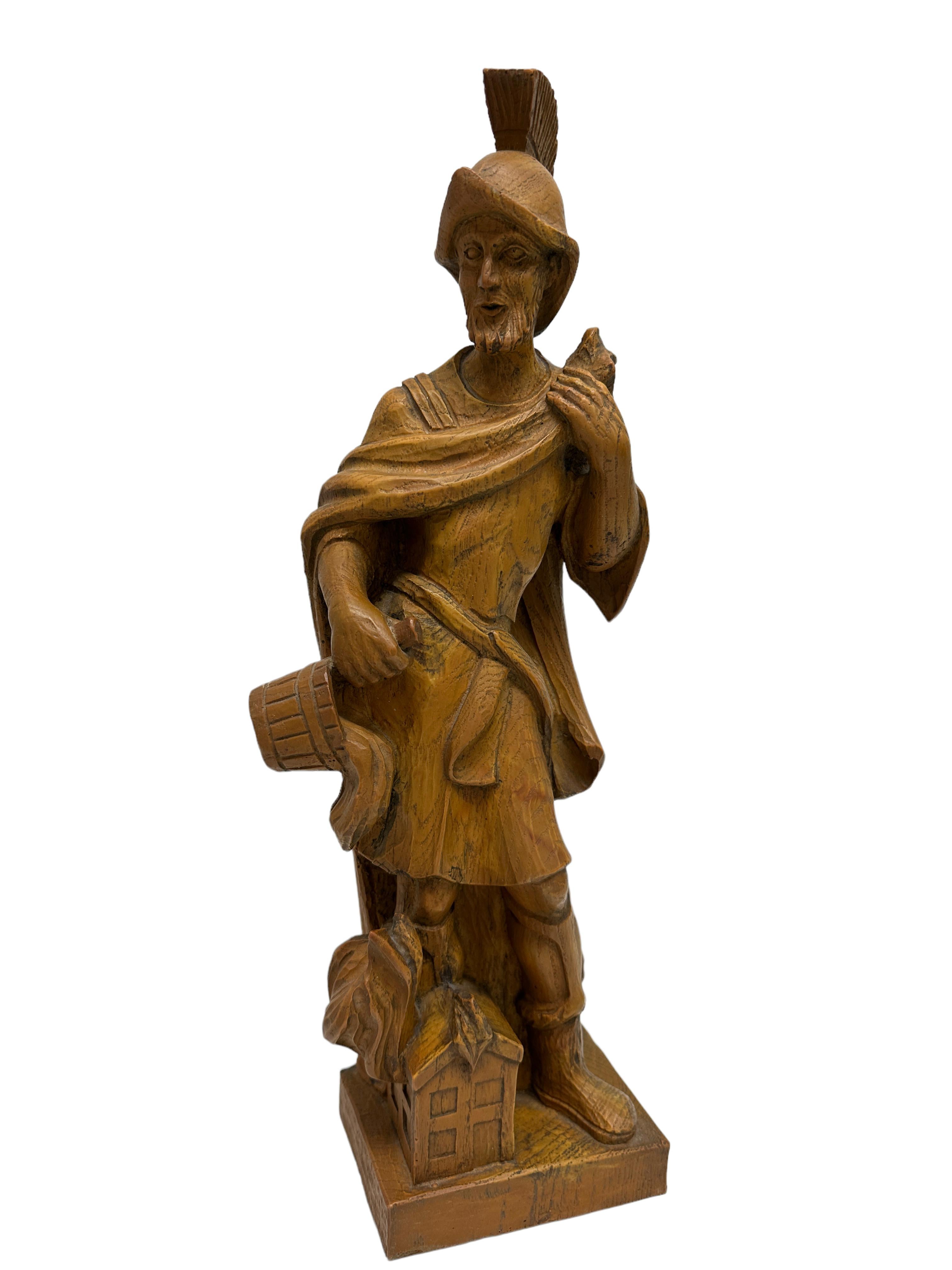 Kieferschnitzerei des Heiligen Florian, des Schutzpatrons der Feuerwehr, Österreich, 20. Jahrhundert, der Heilige hält mit der einen Hand seinen Umhang und schüttet mit der anderen einen Eimer Wasser über ein brennendes Gebäude. Mit einer