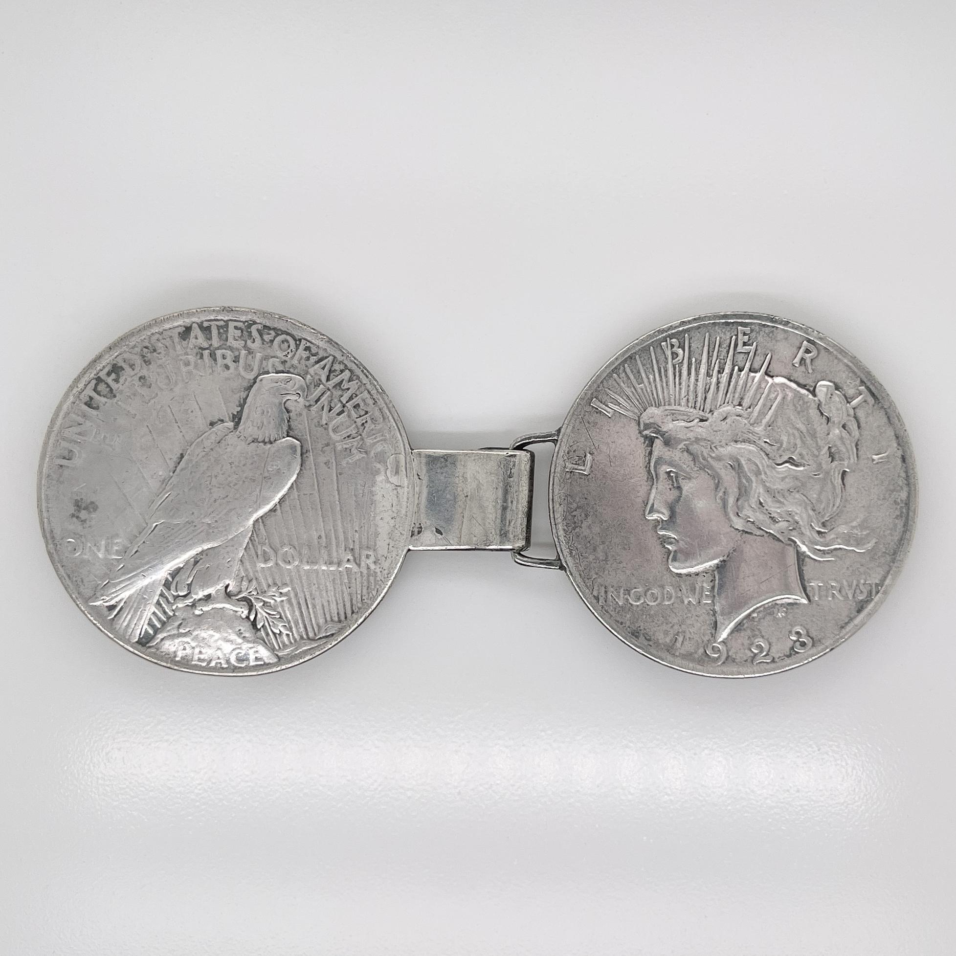 Eine schöne antike Volkskunst Gürtelschnalle.

Bestehend aus 2 Liberty Peace Silberdollarmünzen. Eine ist für 1923 gekennzeichnet.

Jeweils mit einer Schlaufe zur Befestigung eines Gürtels versehen. 

Verschluss mit Öse und Haken. 

Einfach eine