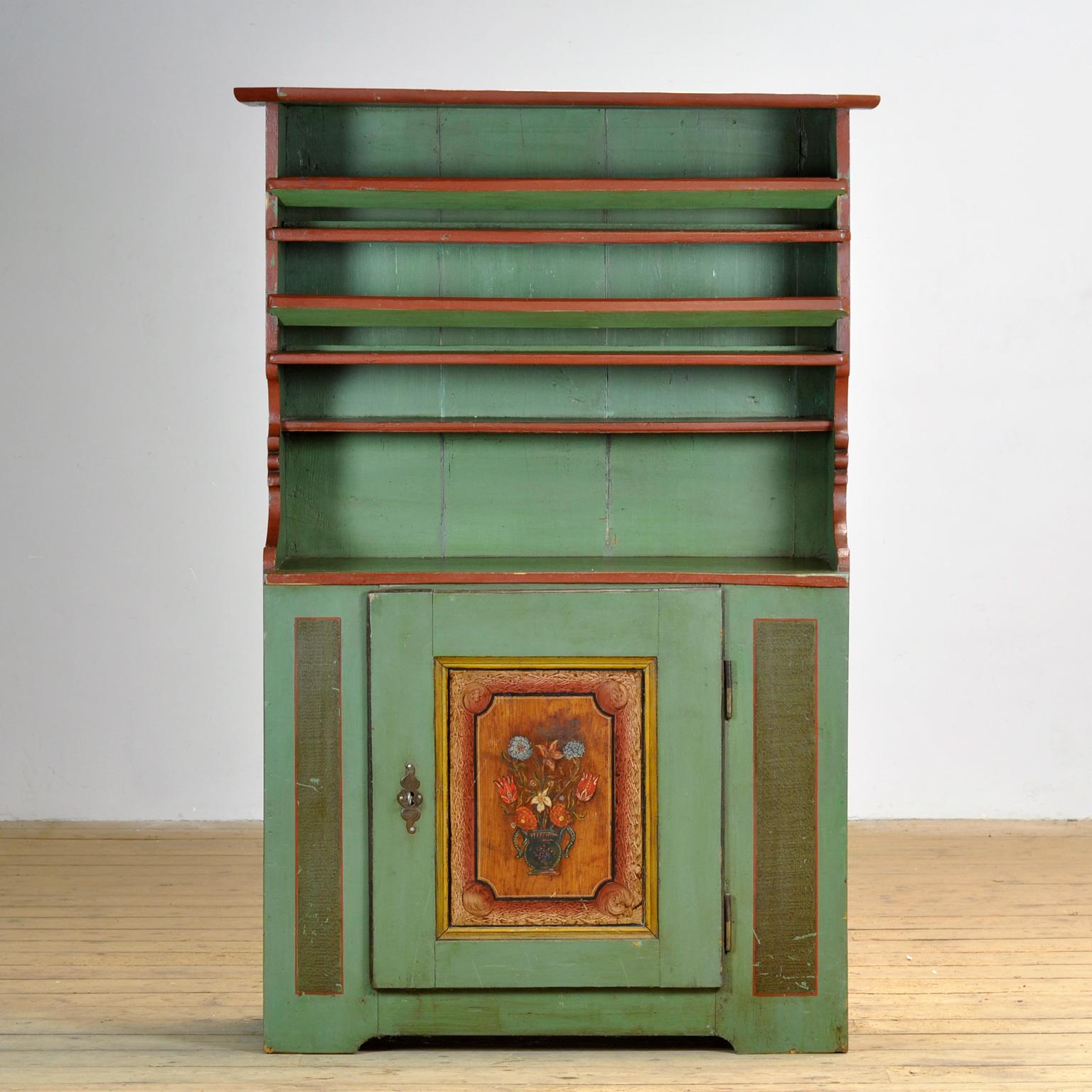 Armoire d'art populaire autrichienne dans une belle nuance de vert, un mélange parfait de fonctionnalité et d'esthétique. Derrière la porte peinte à la main se trouvent deux étagères qui permettent de ranger tous les objets nécessaires. La partie
