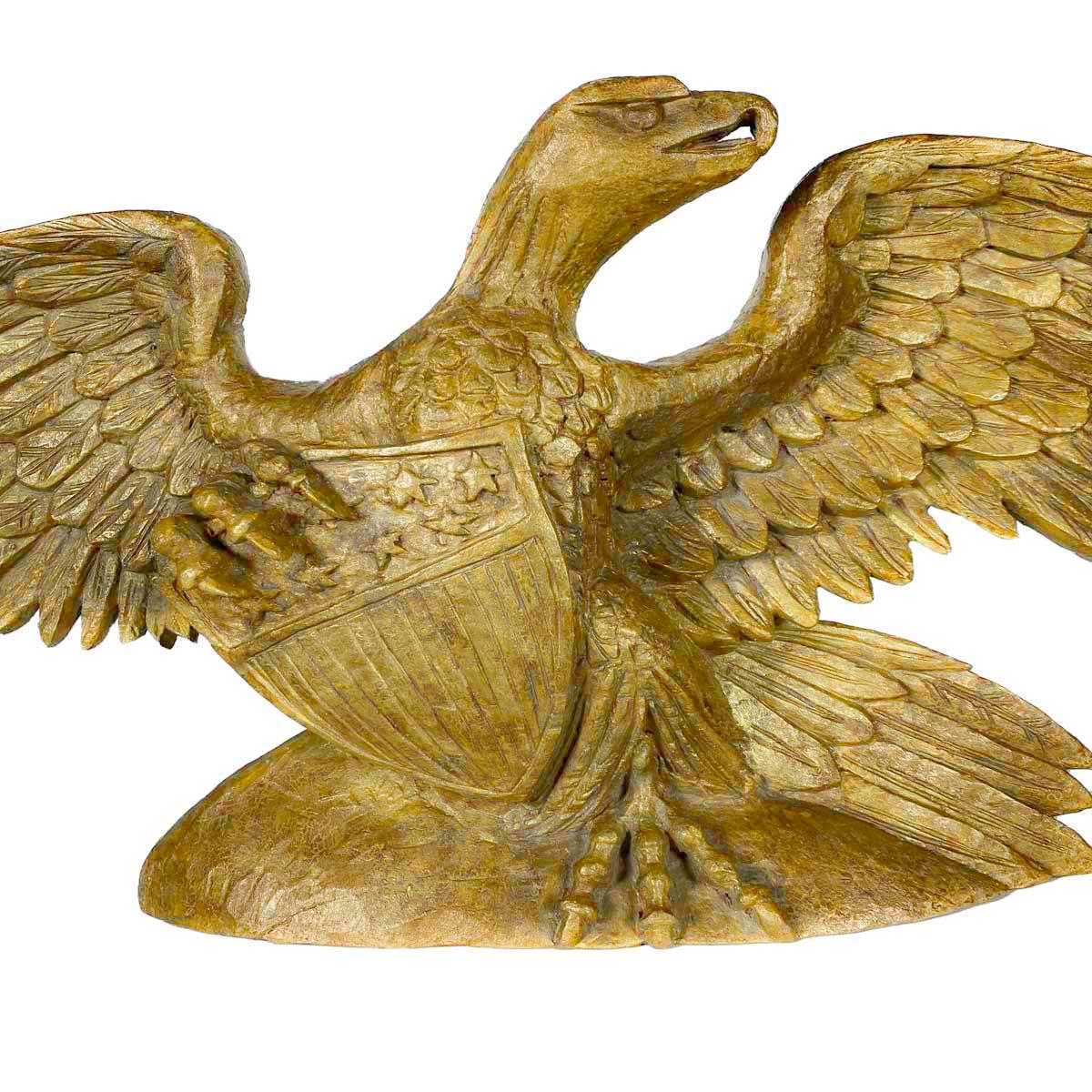 Early 20th century gold painted, carved wood figure of a spread-winged eagle clutching a shield with stars above vertical stripes. The eagle is perched on a rounded base with its head turned and looking fierce.