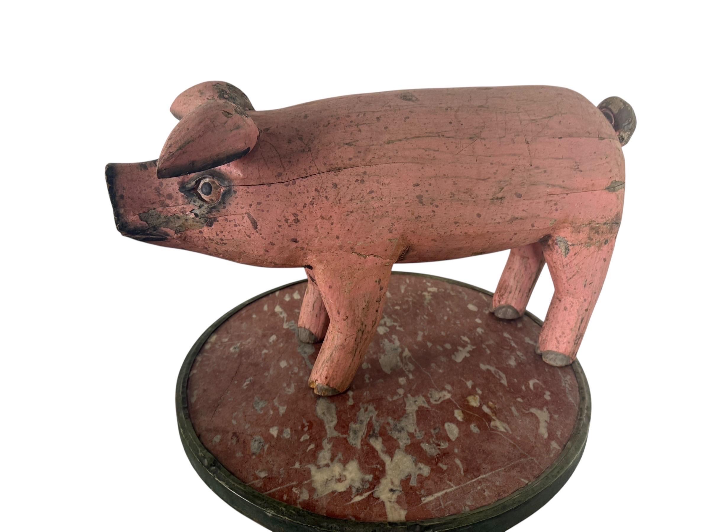 Un affascinante maiale in legno intagliato di arte popolare, dipinto nell'originale rosa tenue con accenti neri. La figura è modellata con un corpo robusto, orecchie erette e coda arricciata, in piedi su quattro zampe robuste. L'intaglio cattura