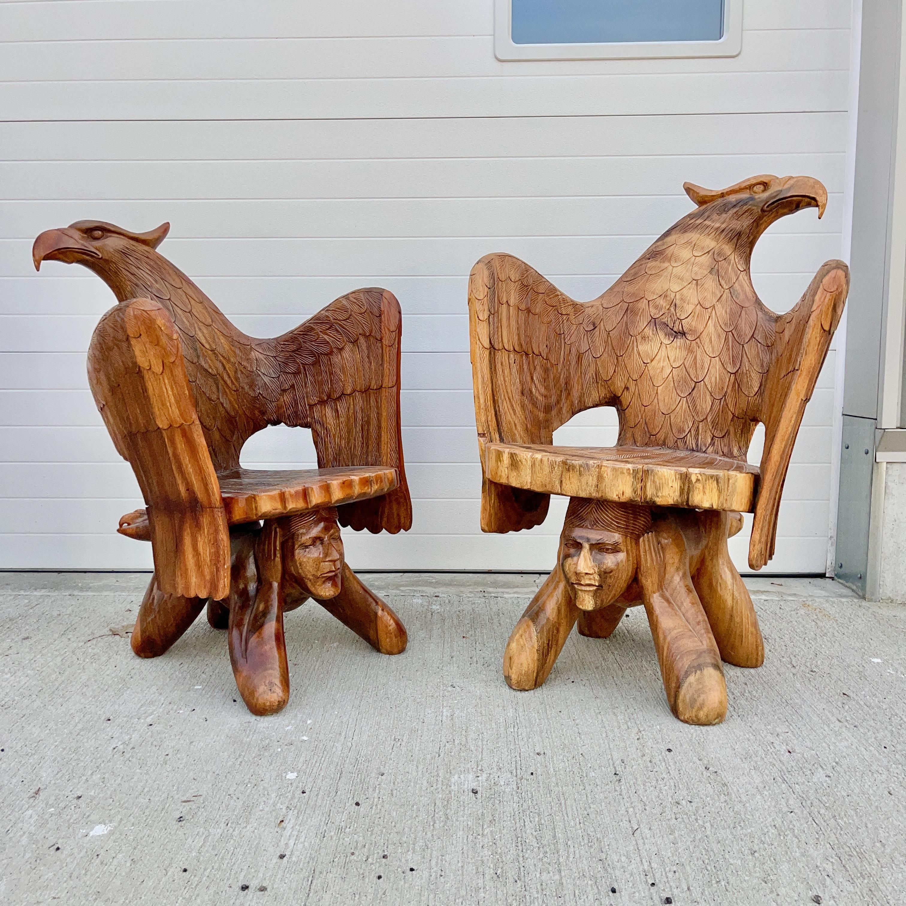 Paire de chaises très inhabituelles, sculptées à la main, peut-être à l'aide d'une tronçonneuse ou d'autres lames, représentant un aigle féroce aux ailes déployées, ses serres sur les pieds d'un homme à quatre pattes tourné vers l'avant sur ses