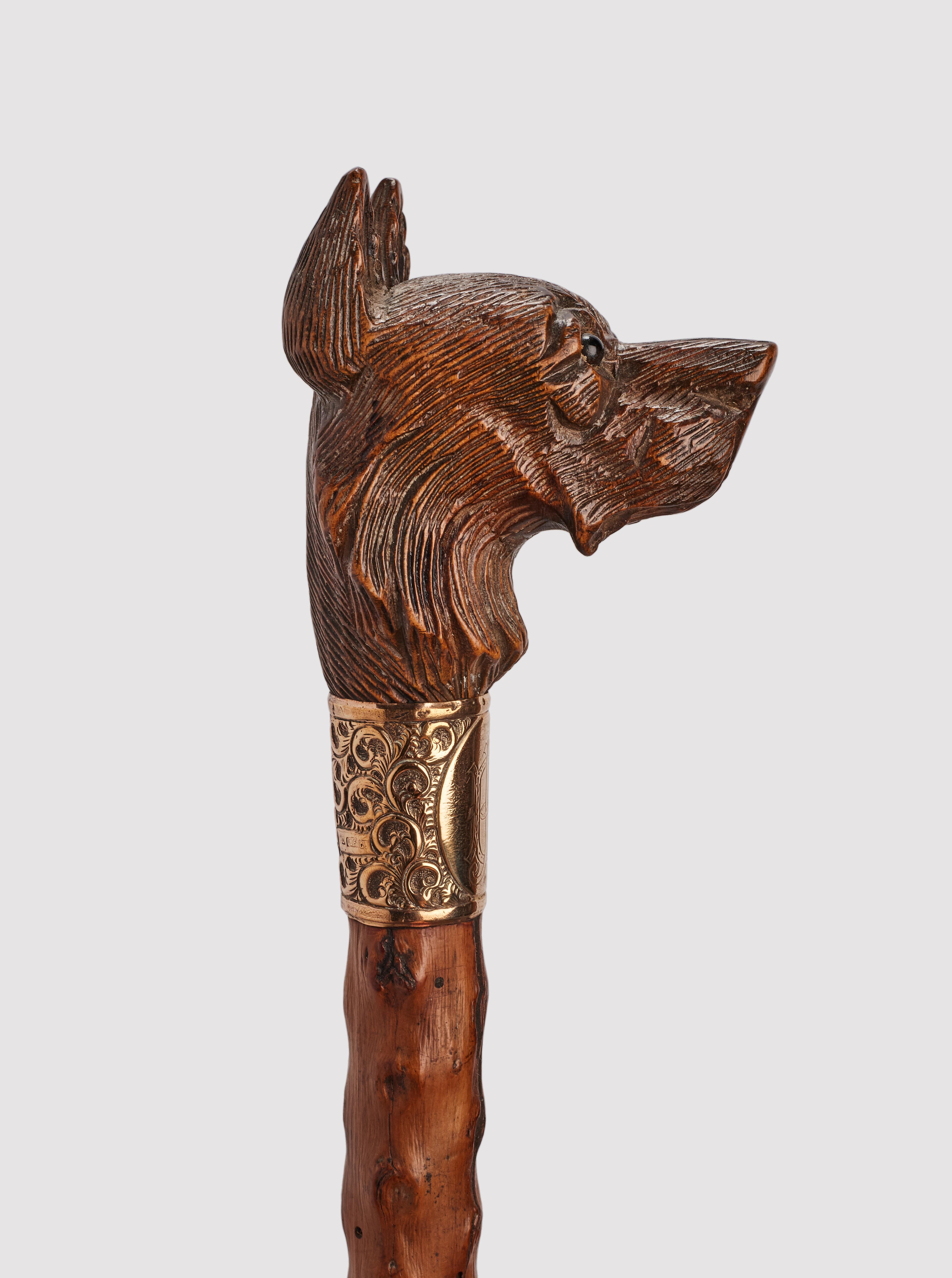 Canne d'art populaire : poignée en bois sculpté représentant une tête de chien de berger allemand, yeux en verre sulfurisé. Manche en bois d'aubépine et virole en métal. Anneau en argent doré. Autriche vers 1890.