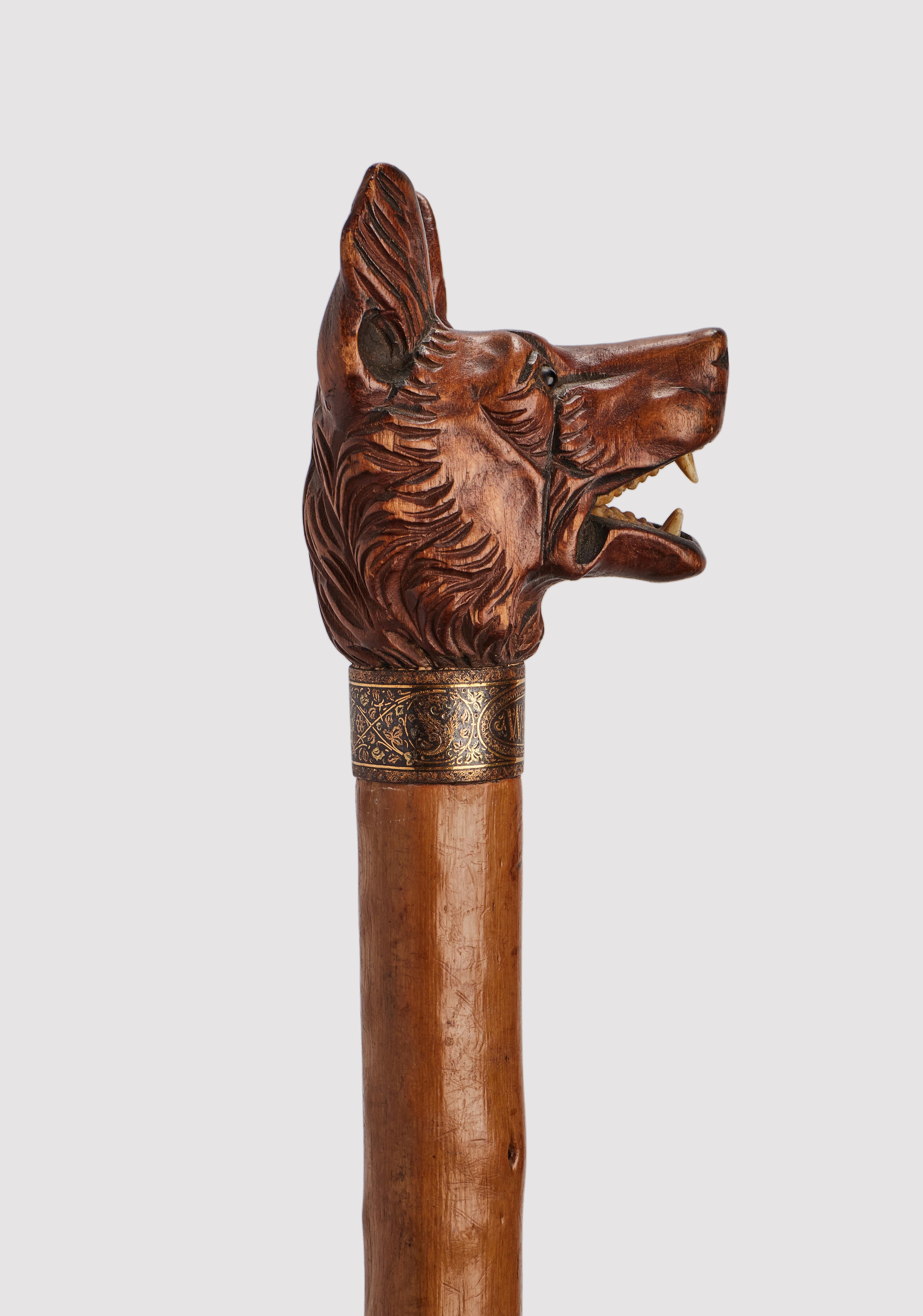 Canne d'art populaire : manche en bois sculpté représentant une tête de chien de berger allemand, yeux en verre sulfureux, dents en os. Manche en bois d'aubépine et virole en métal. Anneau en argent doré. Allemagne vers 1890.