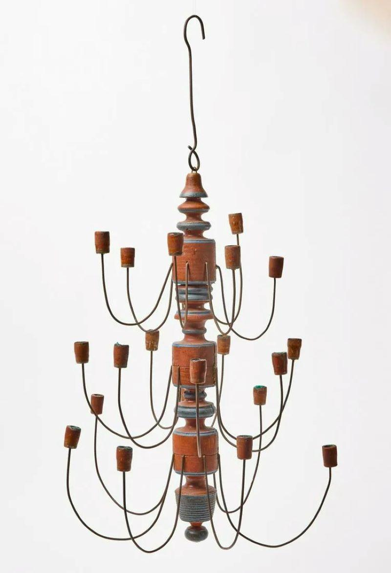 A charming American folk art 21-candle chandelier in turned wood, with blue and rust-red painted finish with wire arms and wood candle holders, circa 1870. Unelectrified.