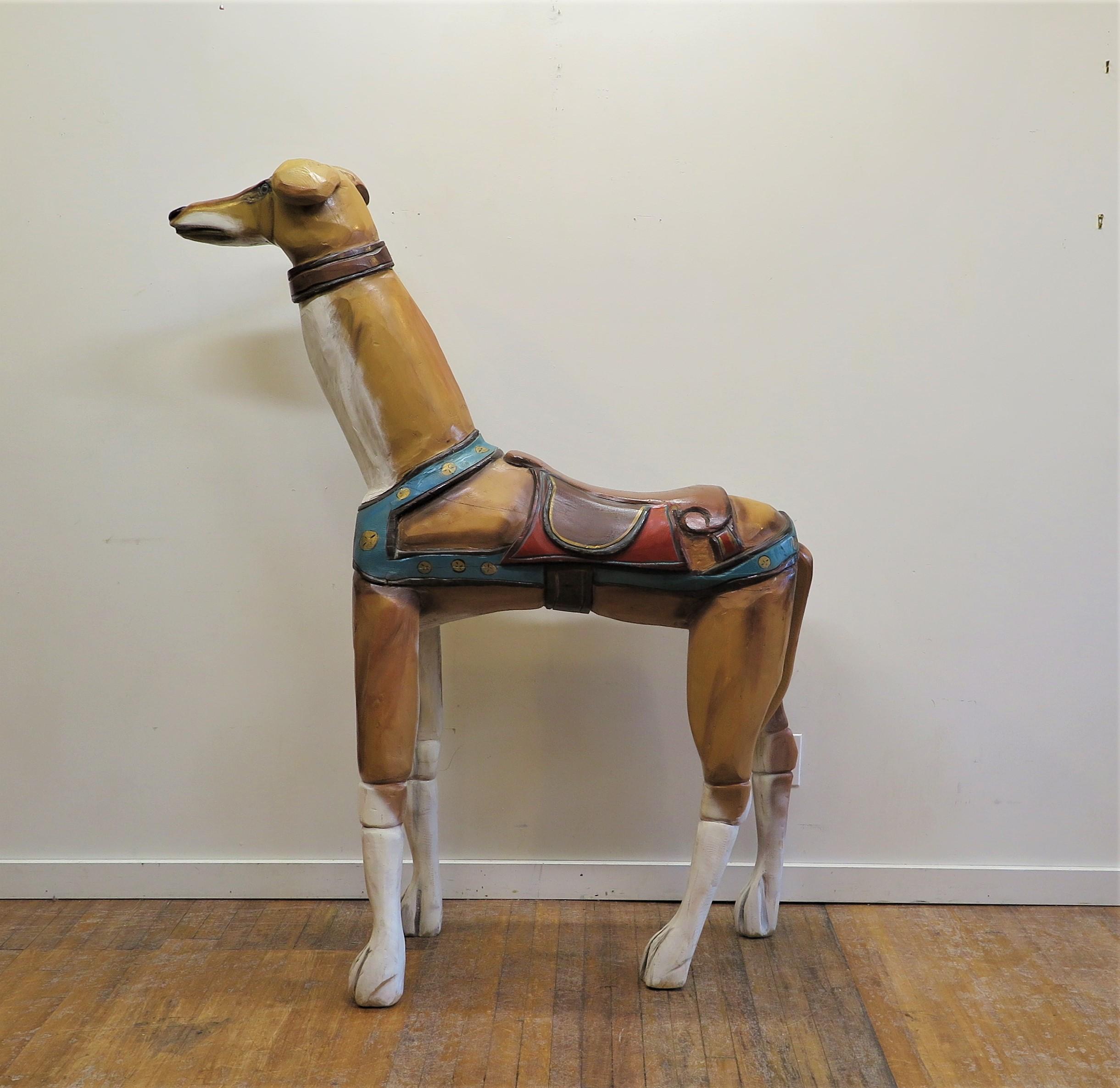 Dog Folk Art sculpture. A life size dog carved out of wood painted, saddled and ready to ride having glass eyes. Whimsical colorful large dog carving depicting a dog saddled for riding. American vintage wood carving sculpture from a grand house