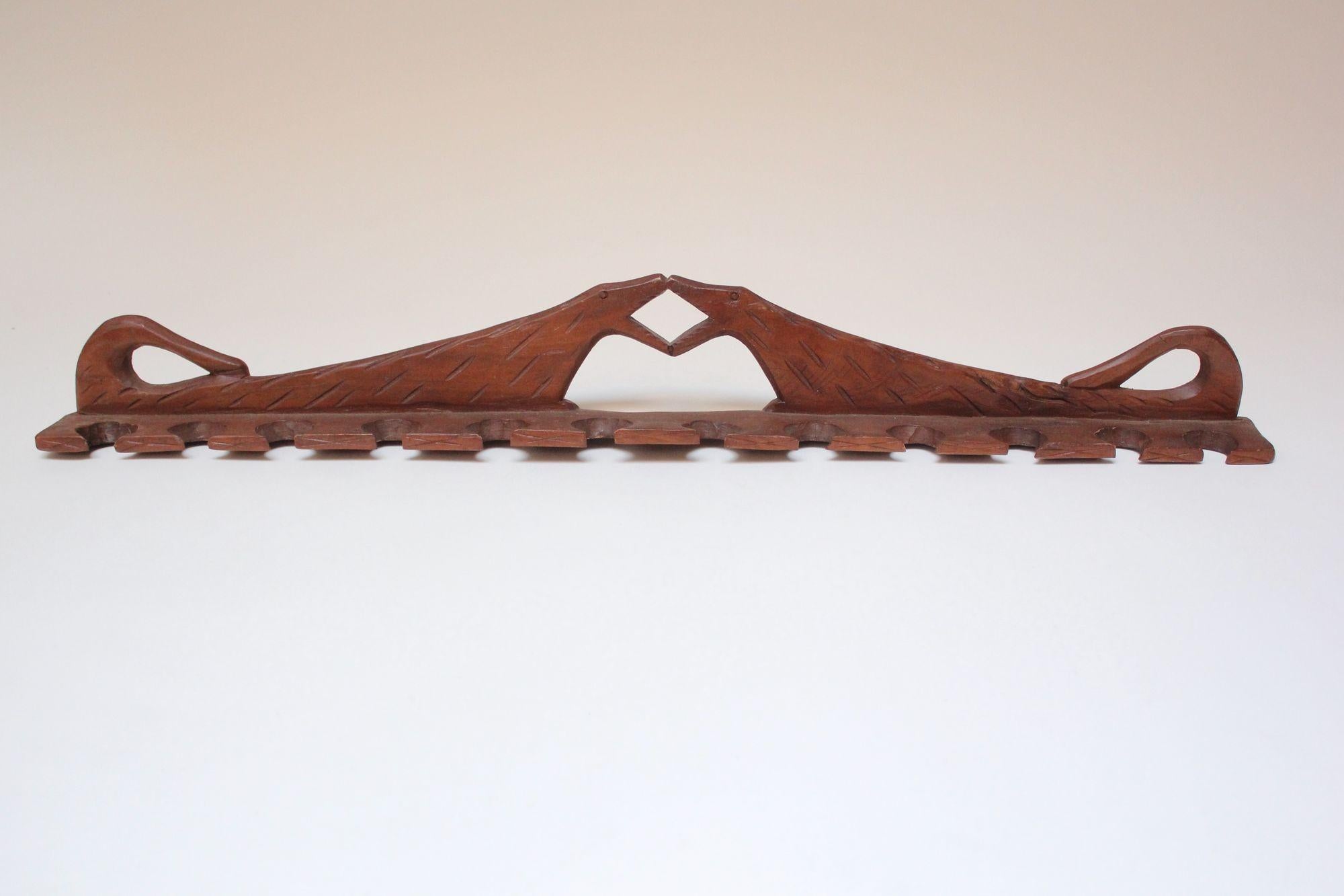 Porte-pipe en bois sculpté à la main avec douze fentes pour les pipes (vers les années 1930, États-Unis).
Conception rudimentaire (les figures elles-mêmes sont, de manière ambiguë, deux chiens qui se rencontrent au niveau des mâchoires).
Belle