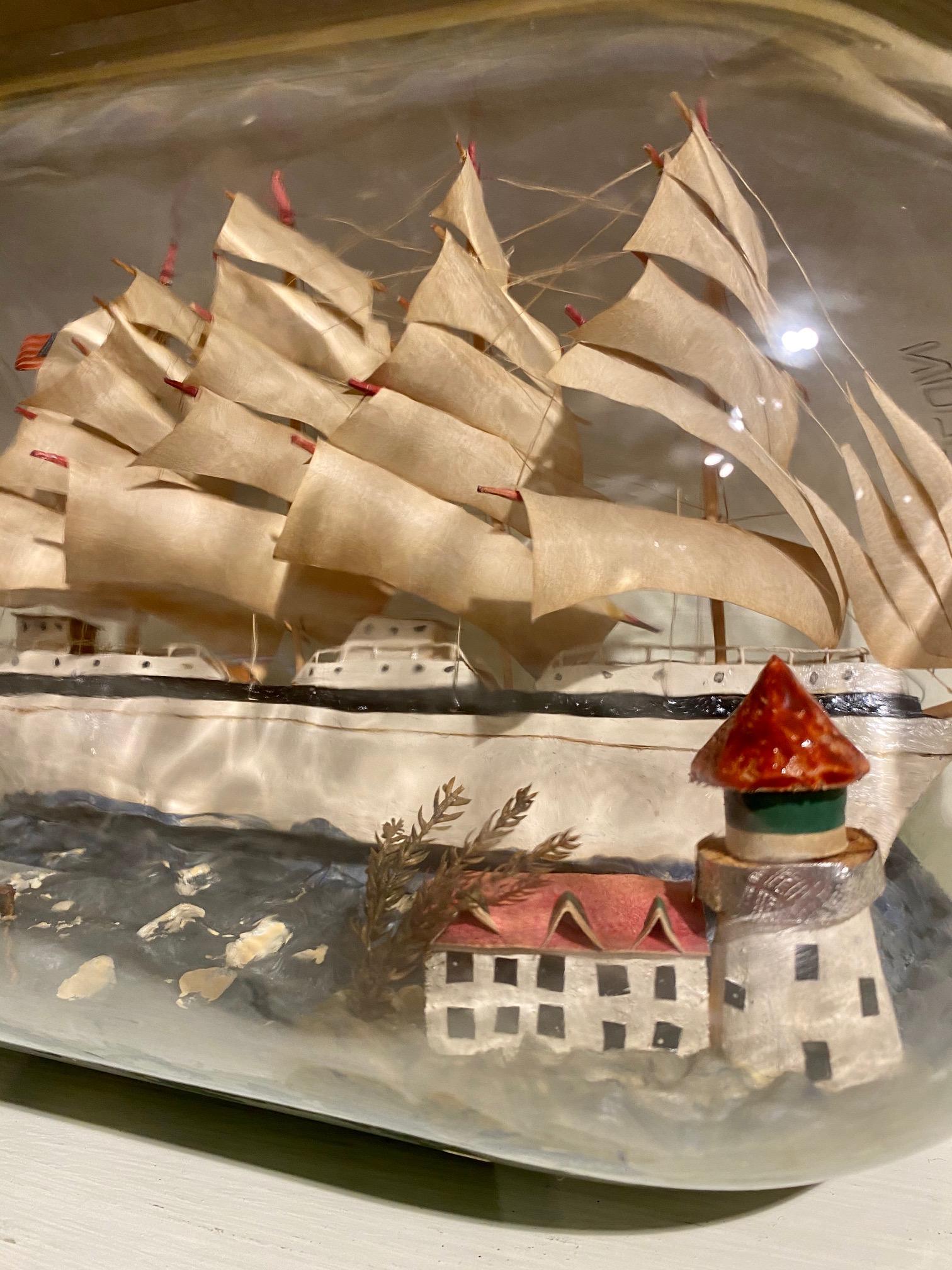 Vintage Folk Art large ship in a bottle, circa 1950s, having a handcrafted diorama with a four-masted Bark and a Sloop sailing past a lighthouse with keeper's cottage and tree. The model is made with a hand carved hull and paper sails set on stick