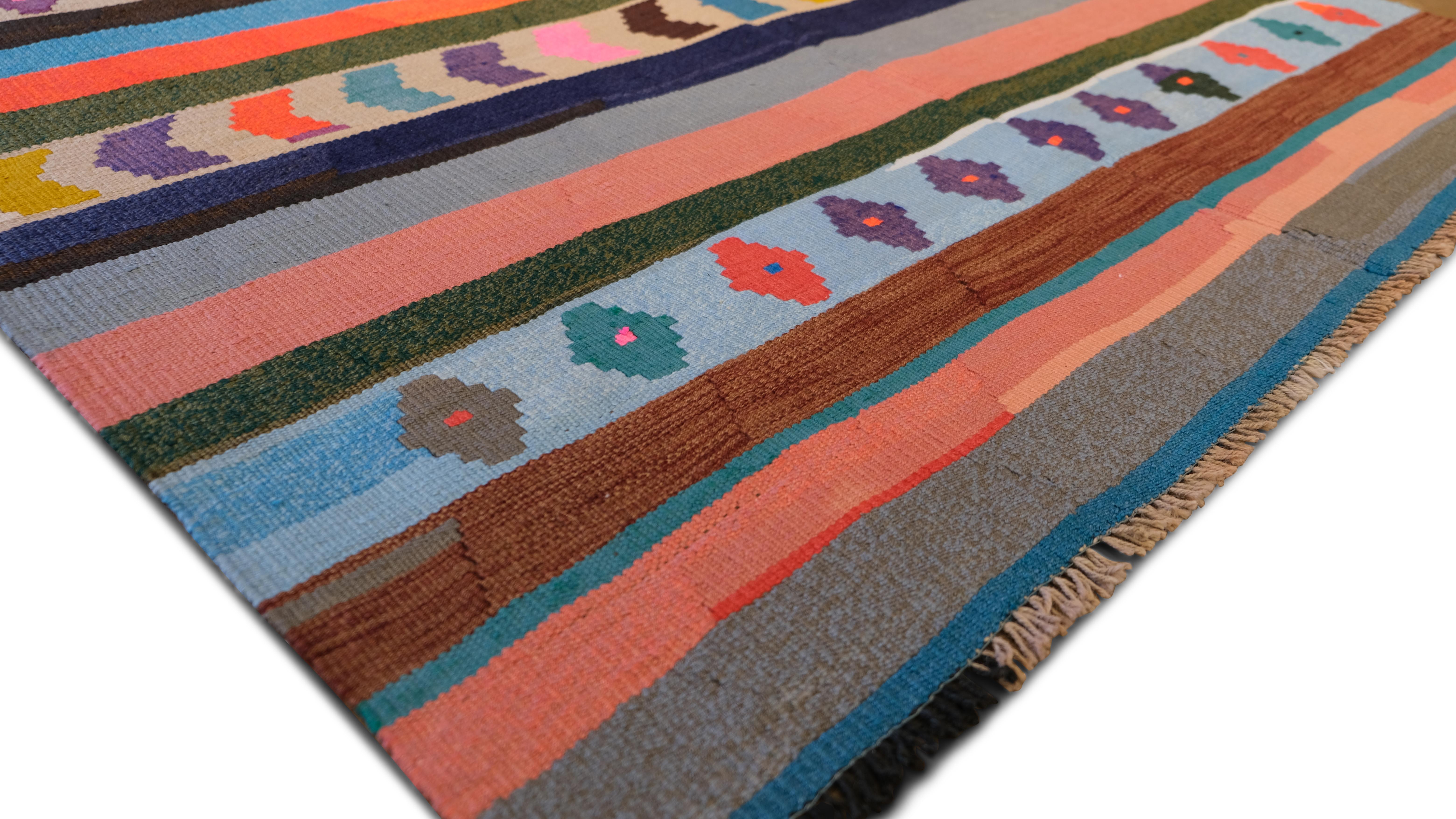 Ce kilim en laine tissé à la main présente un motif géométrique rayé audacieux dans une palette multicolore vivante, reflétant les riches traditions de tissage de la région. Les motifs complexes en chevron, les médaillons en diamant et les bandes