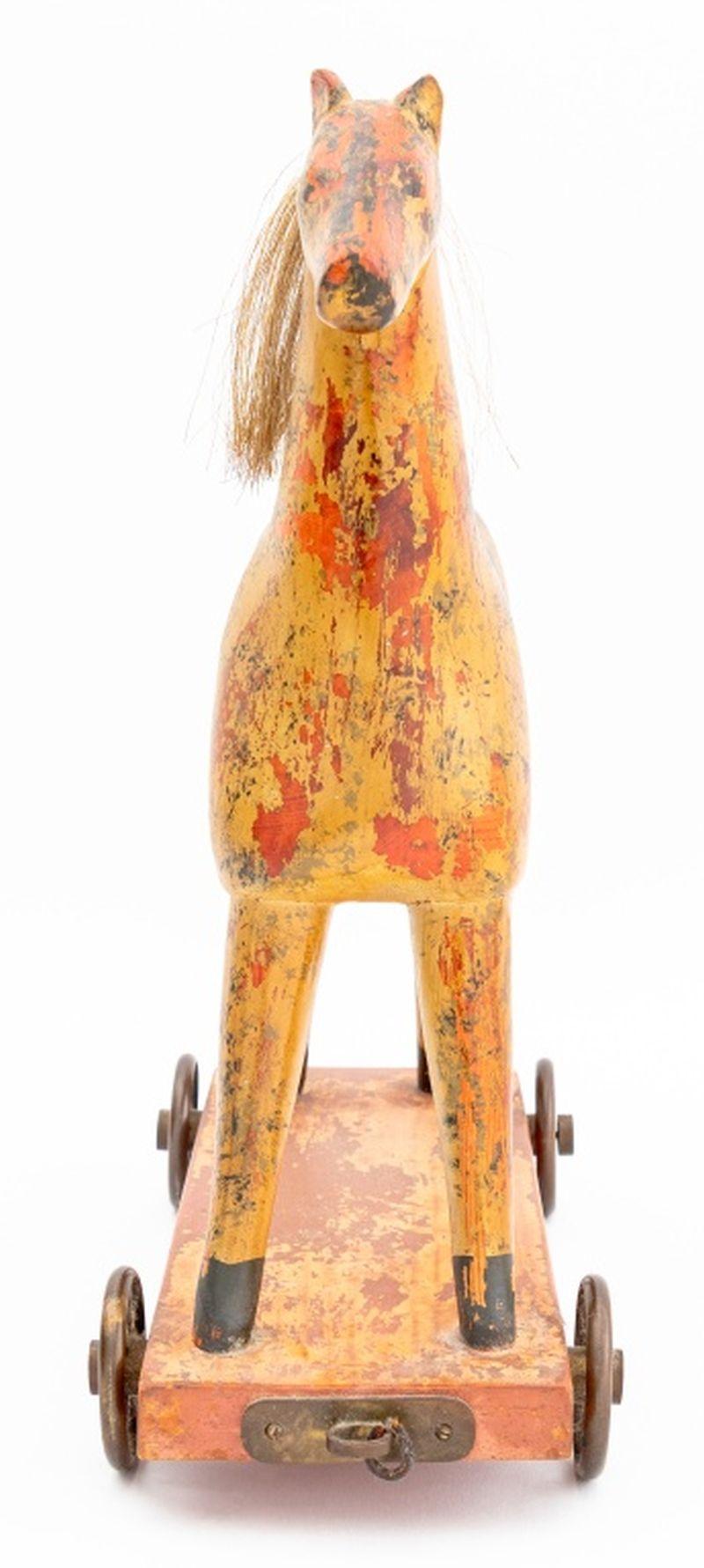 Groupe de deux jouets en bois peints d'art populaire, comprenant : un cheval à tirer, 1983, monté sur une base rectangulaire et quatre roues en métal, marqué 