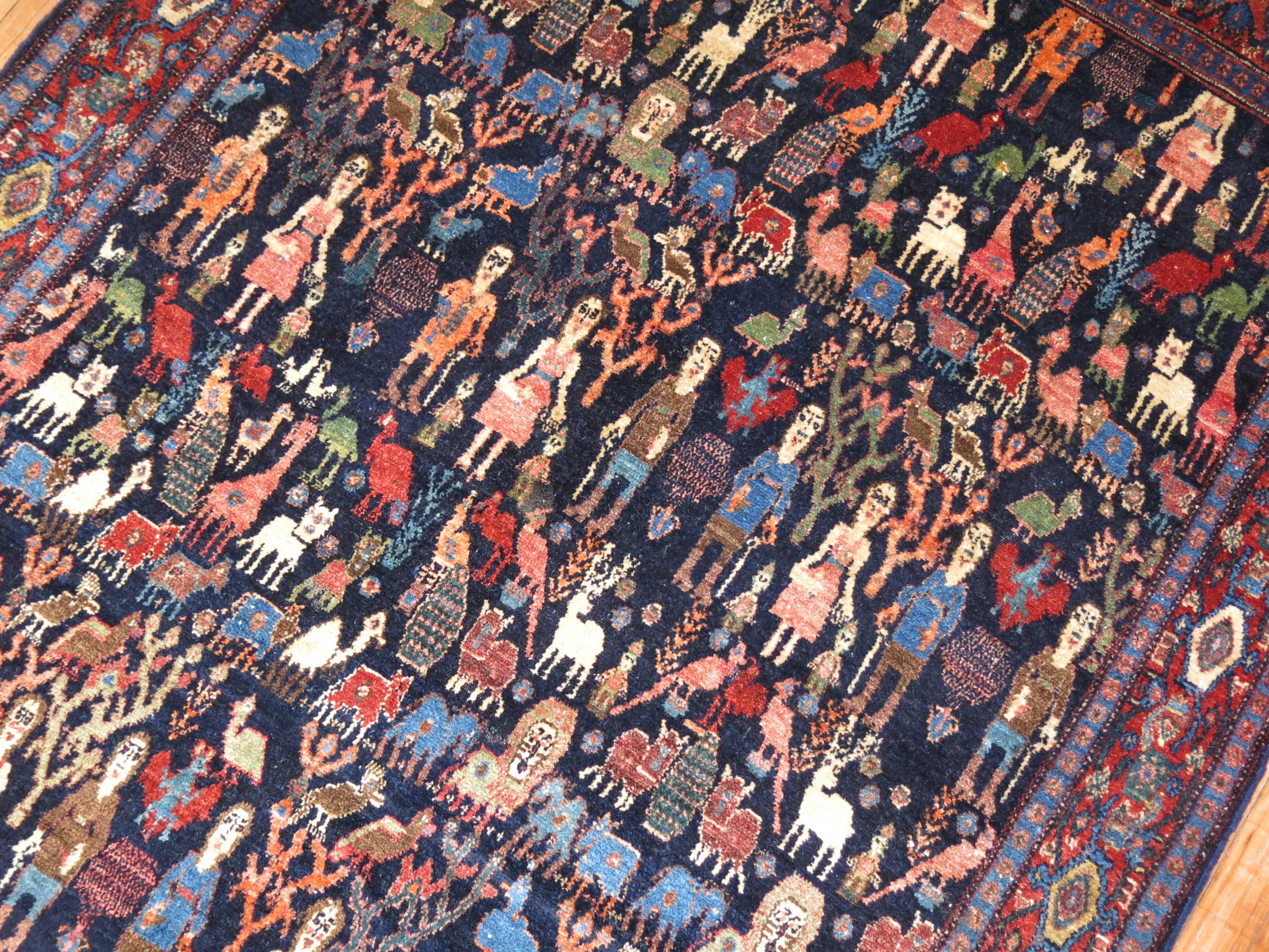 This is a rare quirky early 20th century Persian Senneh Weave rug featuring an array of animals and humans on a dark navy blue ground. What makes this rug so interesting is 1 end of it has humans with heads missing on 1 end of the rug which was