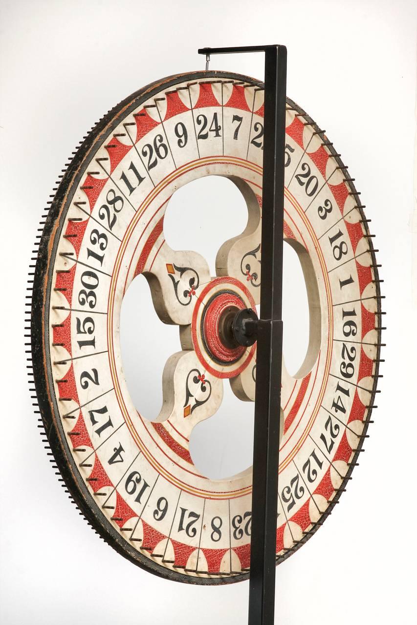 Americana Folk Art carnival game wheel rescued from Santa Monica Pleasure Pier in California. Features a hand-decorated double sided wheel with a craquelure patina finish. Beautifully displayed by a wrought iron stand with four scrolled feet.
