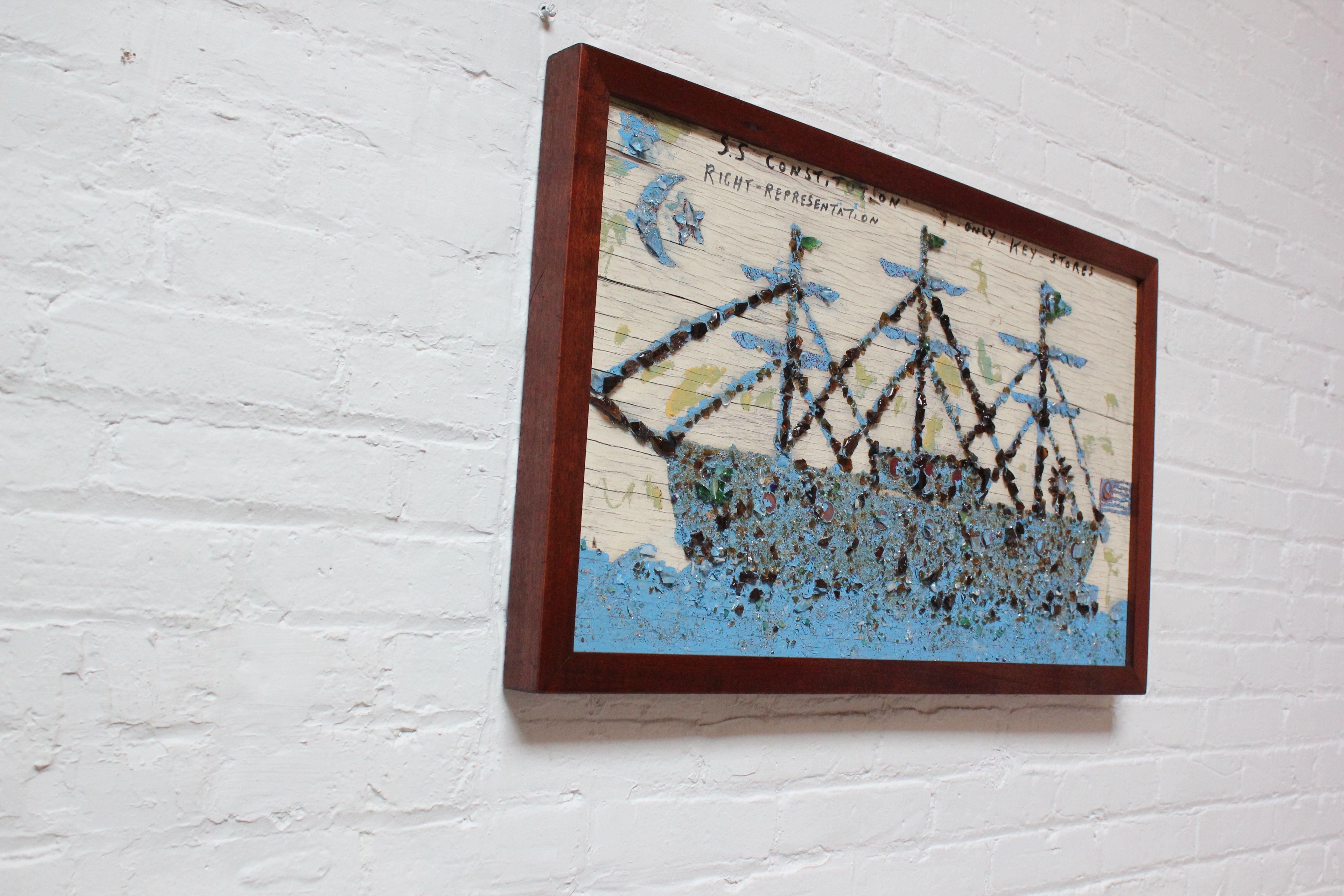Folk Art depiction of the USS Constitution composed of cut sea glass mosaic with copper coin decorative accents and hand-painted details on wooden board (ca. 1970s, USA). The text at the top reads: SS - Constitution Right-Representation - Only Key