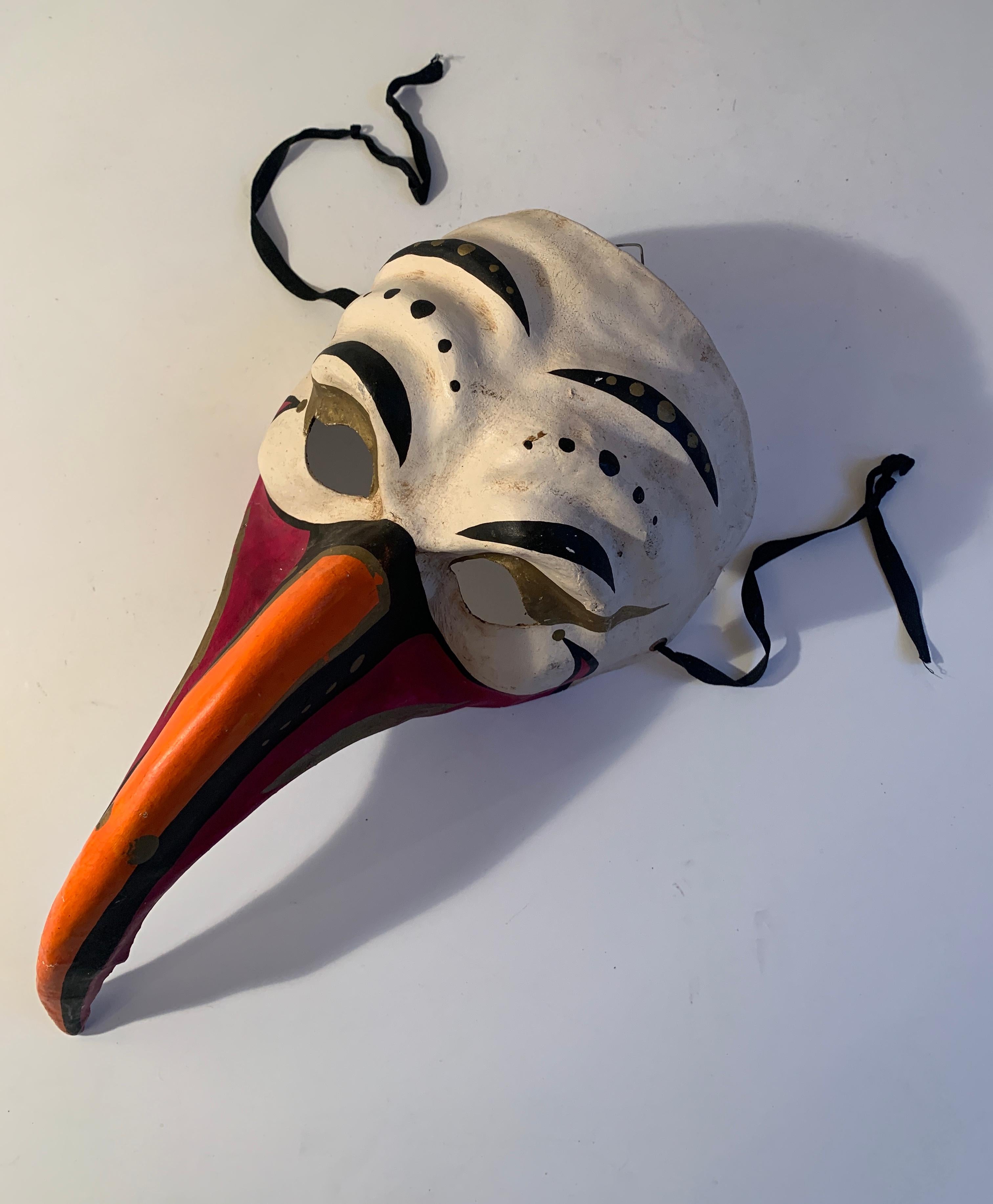 A colorful and unique papier mâché Venetian Mask. Uniquely crafted with molded exaggerated features and long beak enhanced with hand painted colorful combination of orange, black and gold detailing. 

Perfect for everything from sitting on a